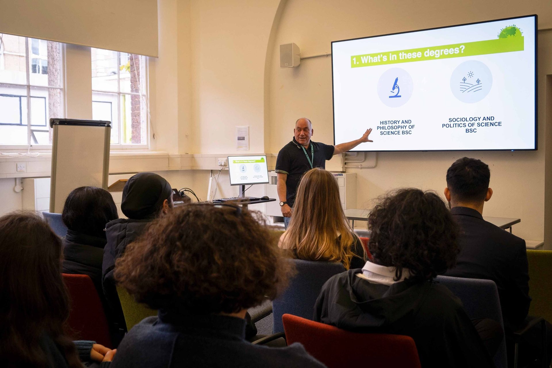 A lecturer points at a screen with degree information to a diverse group of students in a classroom.