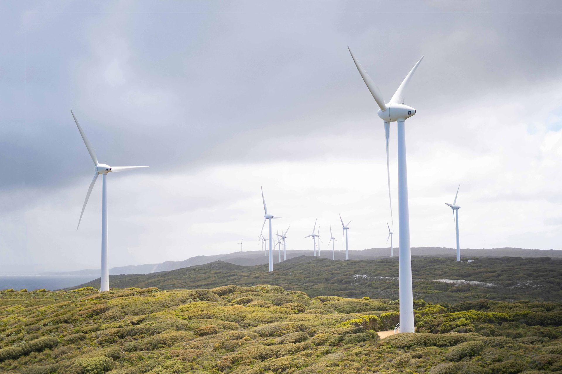 Wind farm on green hills with a cloudy sky.