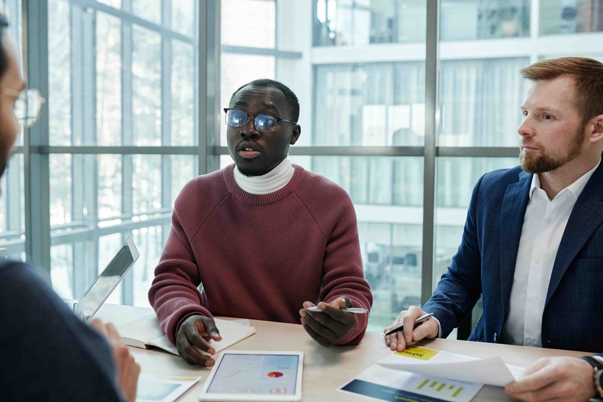 Three men in a modern office having a business meeting or discussion at a table with a tablet.