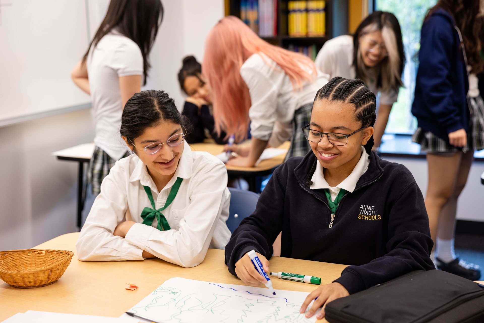 Two smiling female students drawing at a desk in a classroom.