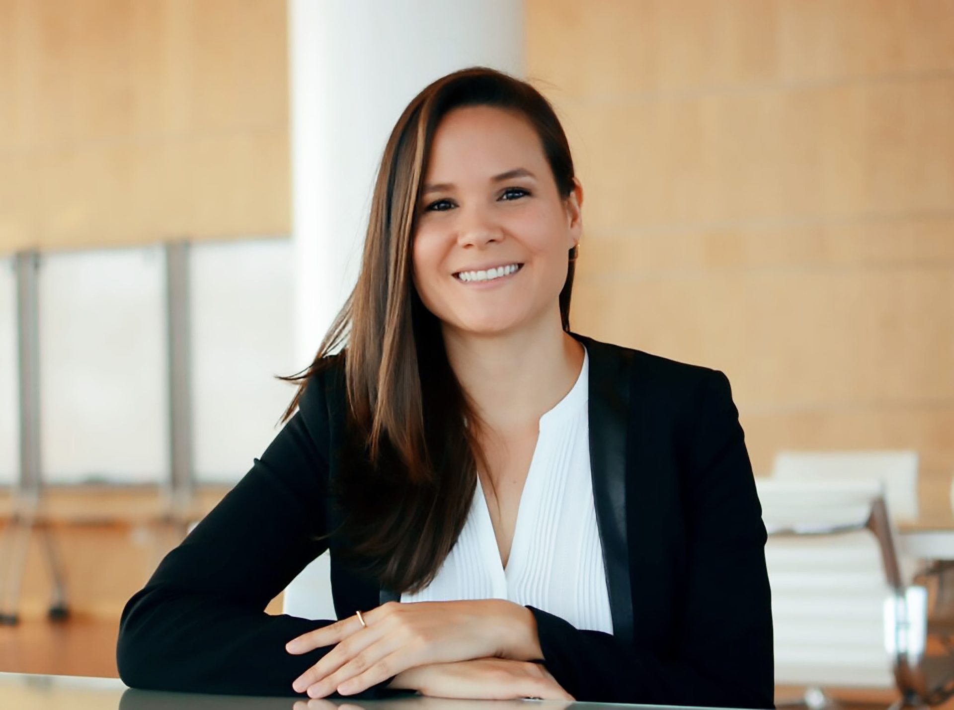 Smiling woman in black blazer, hands clasped.