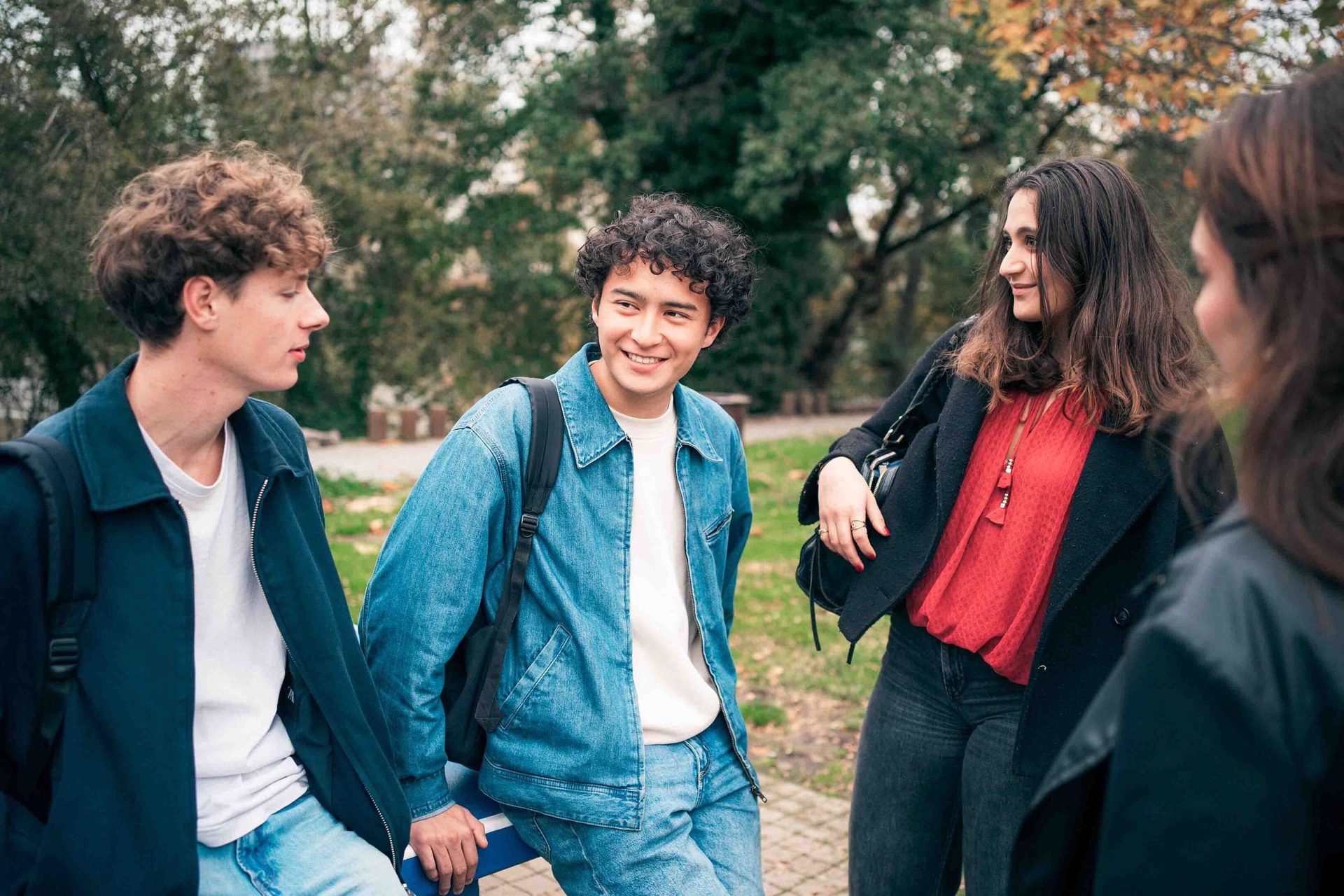 Four young people, three clearly visible, gathered outdoors, engaged in conversation. One man smiles.