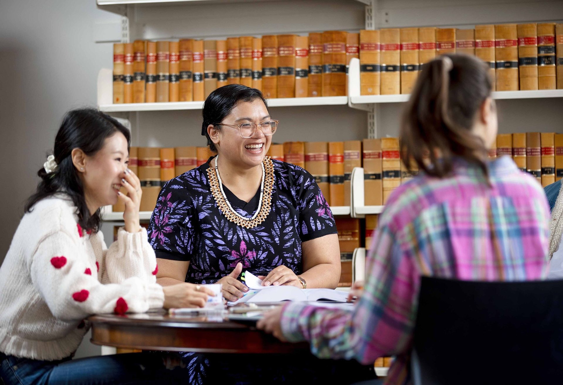 Three smiling women discussing at a table in a library.