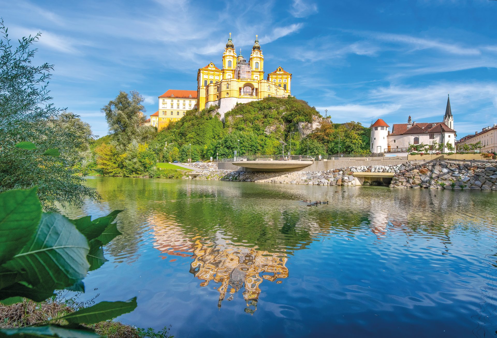 Melk Abbey, a magnificent baroque monastery on a hill, reflected in the river with a blue sky.