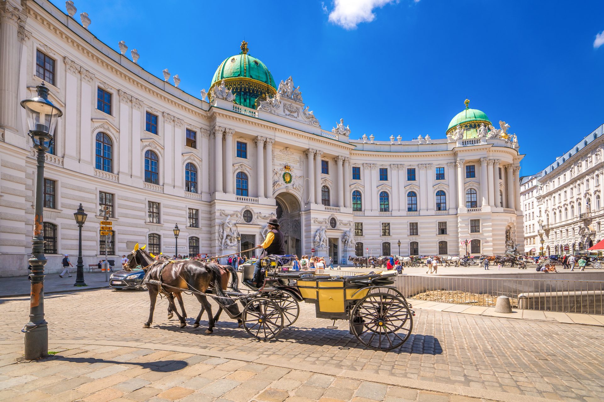 A horse-drawn carriage in front of the Hofburg Palace in Vienna on a sunny day.