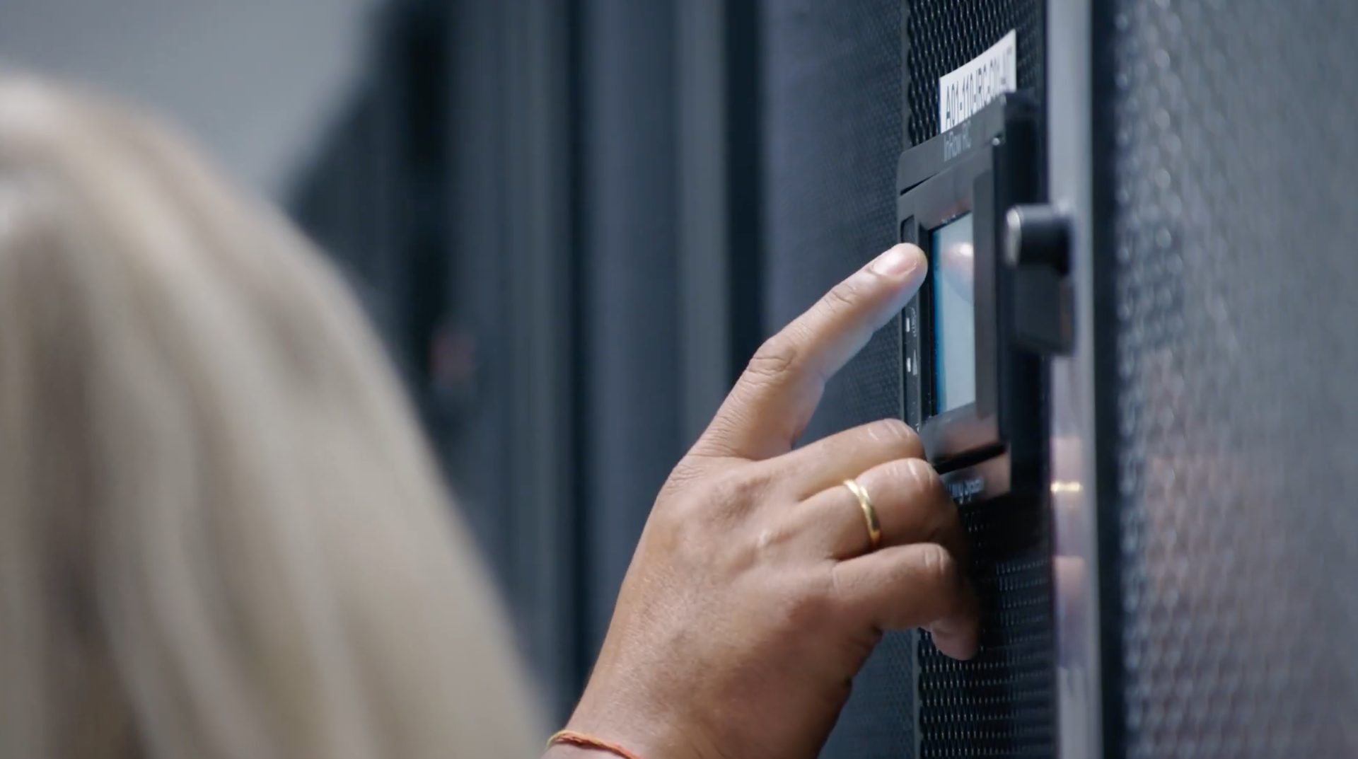A hand with a ring touching a screen on a server or data center unit.