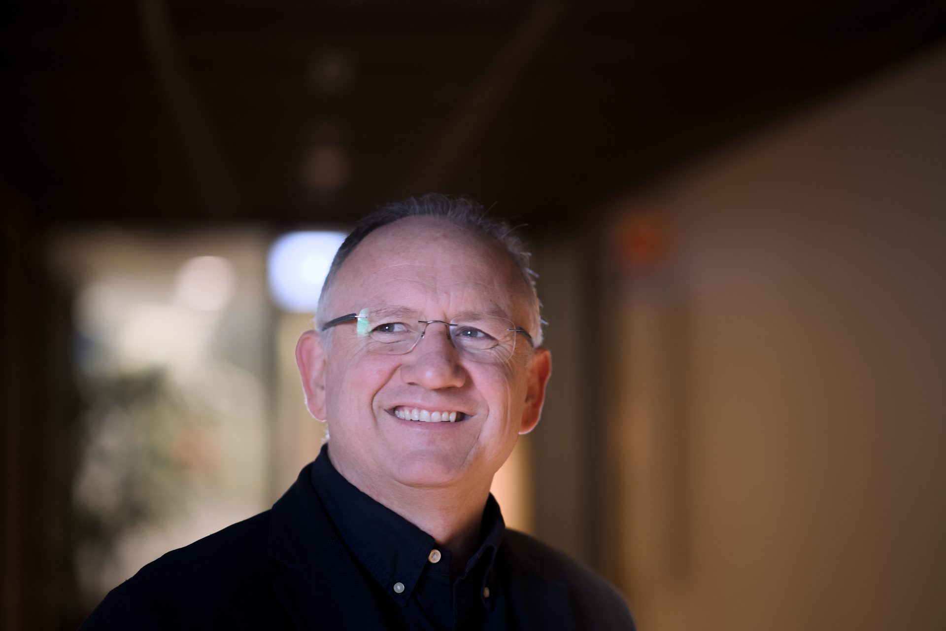 A smiling man with glasses and a dark shirt looks up to the right.