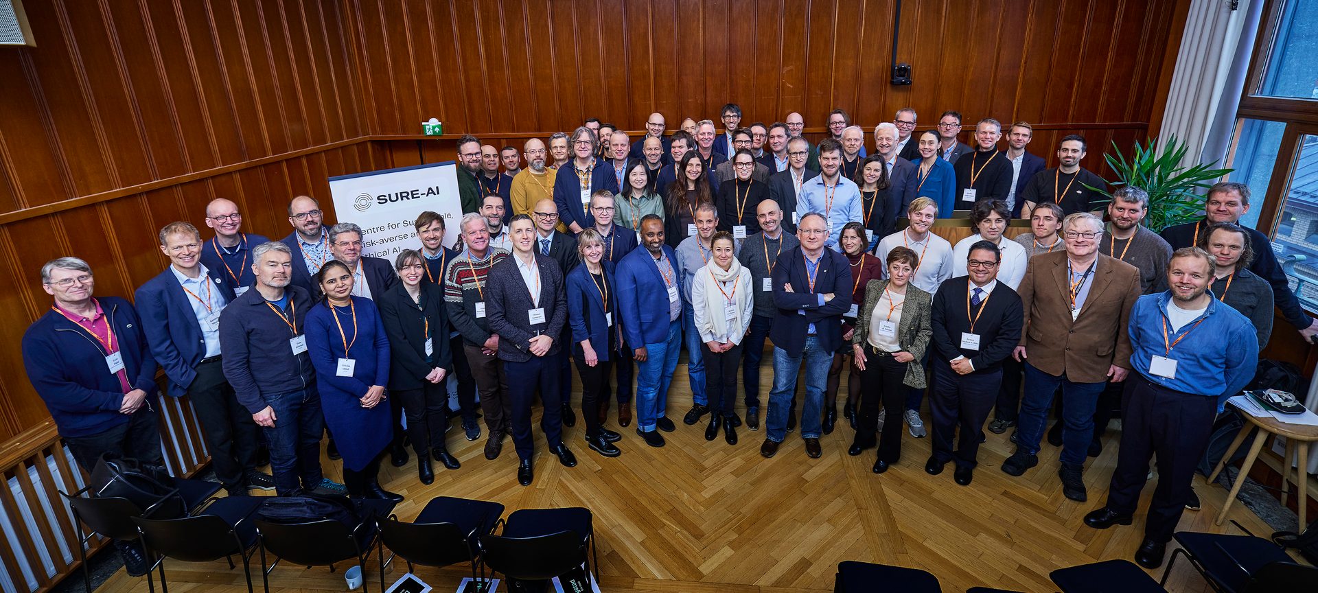 A large group of people at an indoor event, a "SURE-AI" banner is visible.