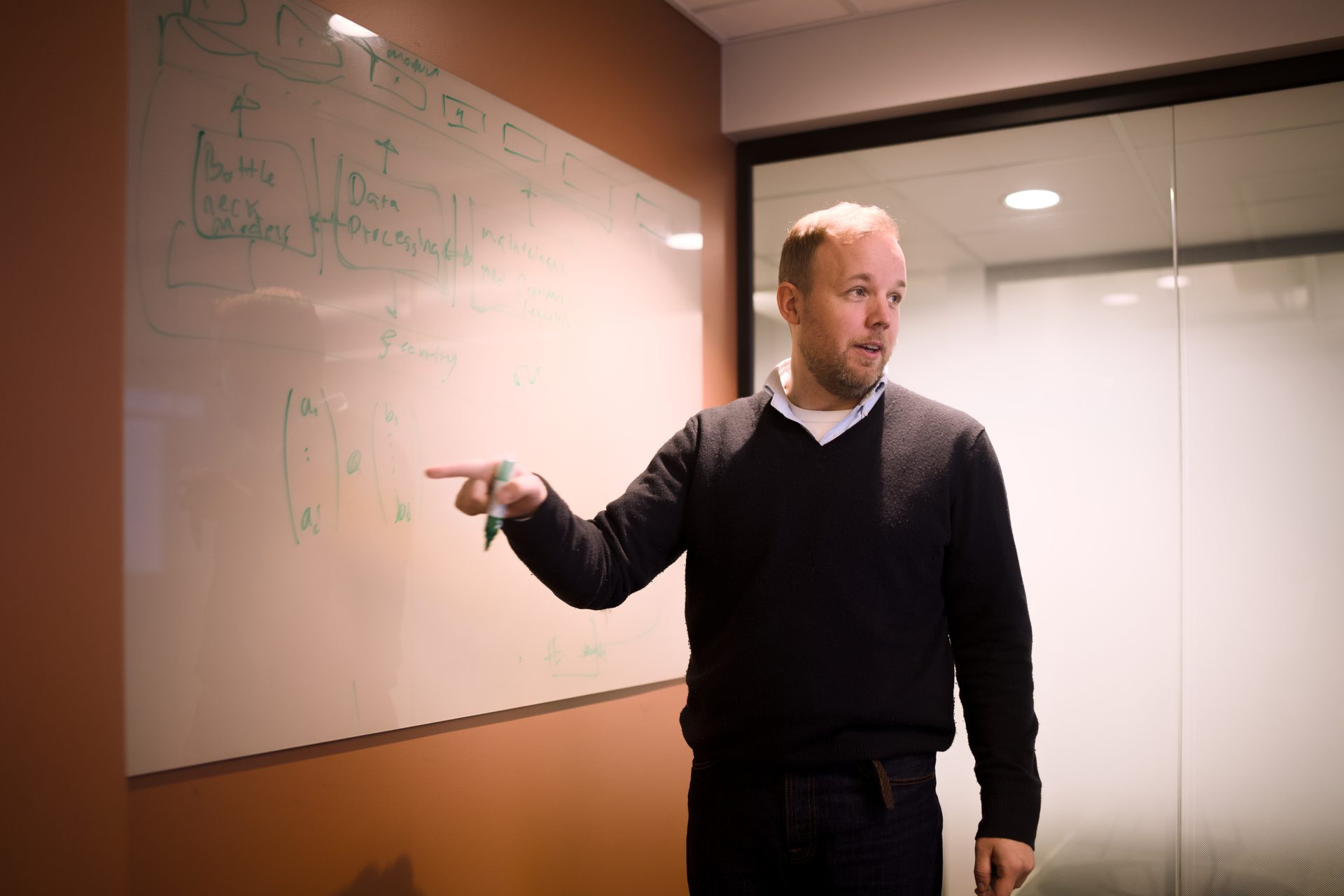 Man pointing at a whiteboard with diagrams and equations.