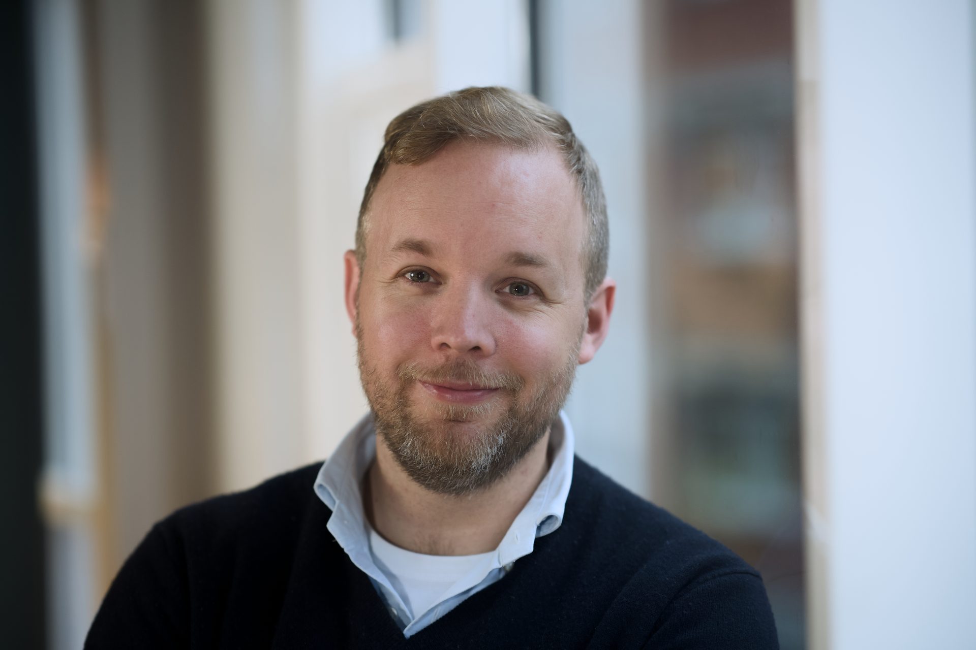 Close-up of a smiling man with a beard in a dark sweater and collared shirt.