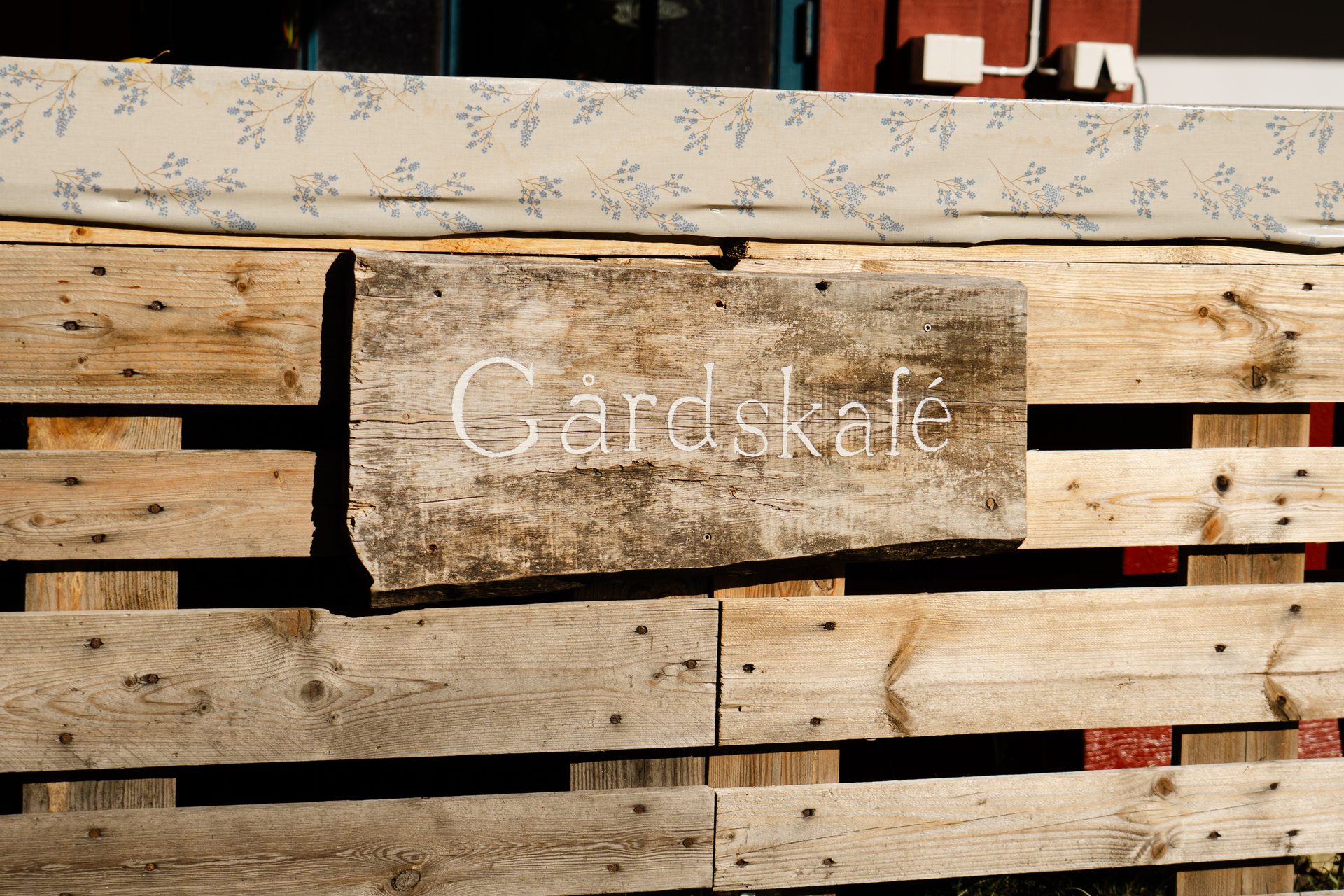 "Gårdskafé" sign on a wooden pallet fence with patterned fabric above.