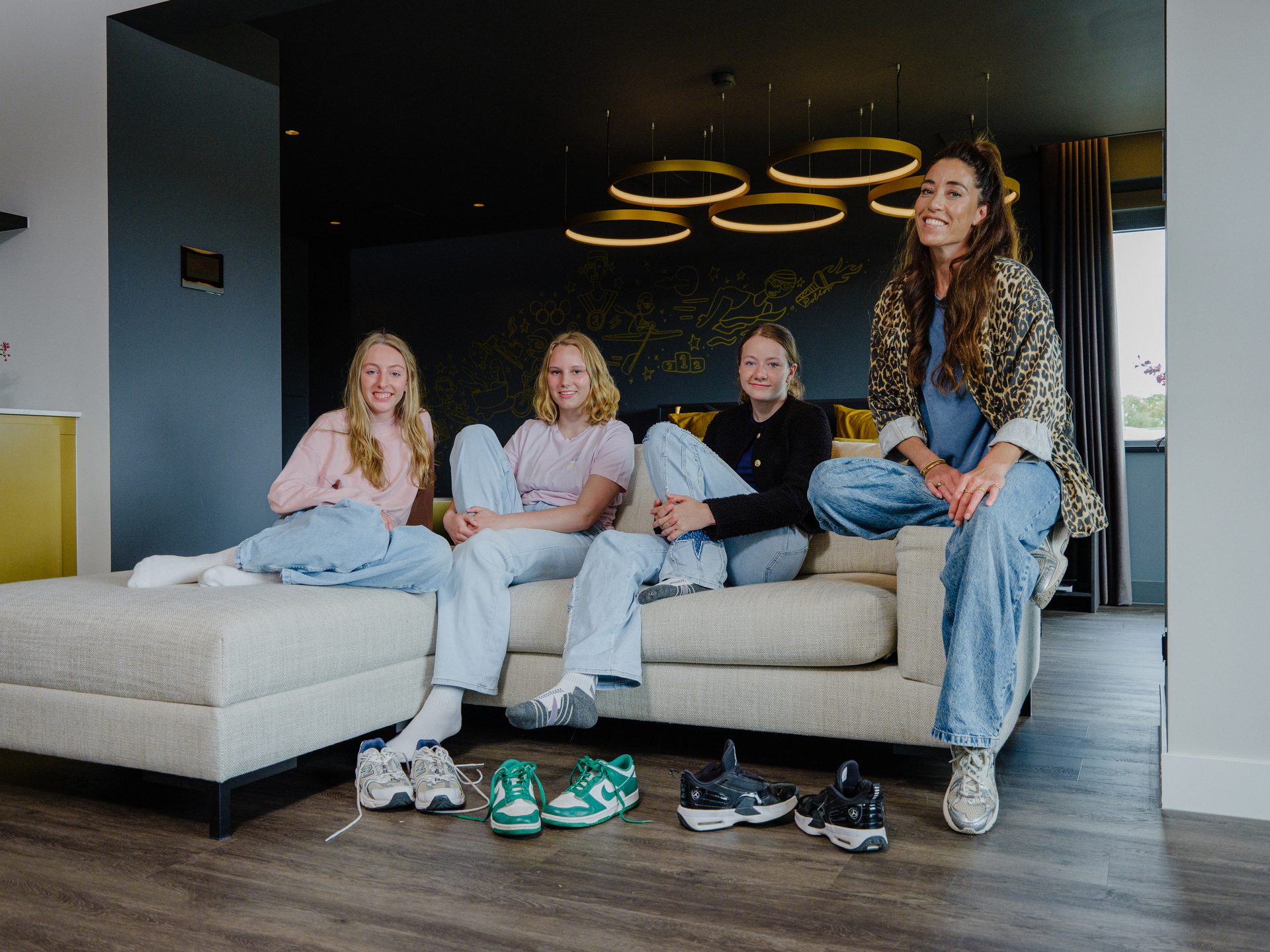 Four smiling women on a couch with shoes on the floor.