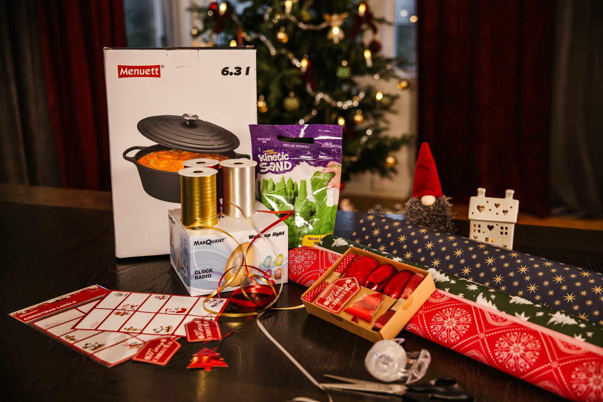 Christmas gifts & wrapping supplies: pot, Kinetic Sand, clock radio, paper, ribbons, labels, gnome.