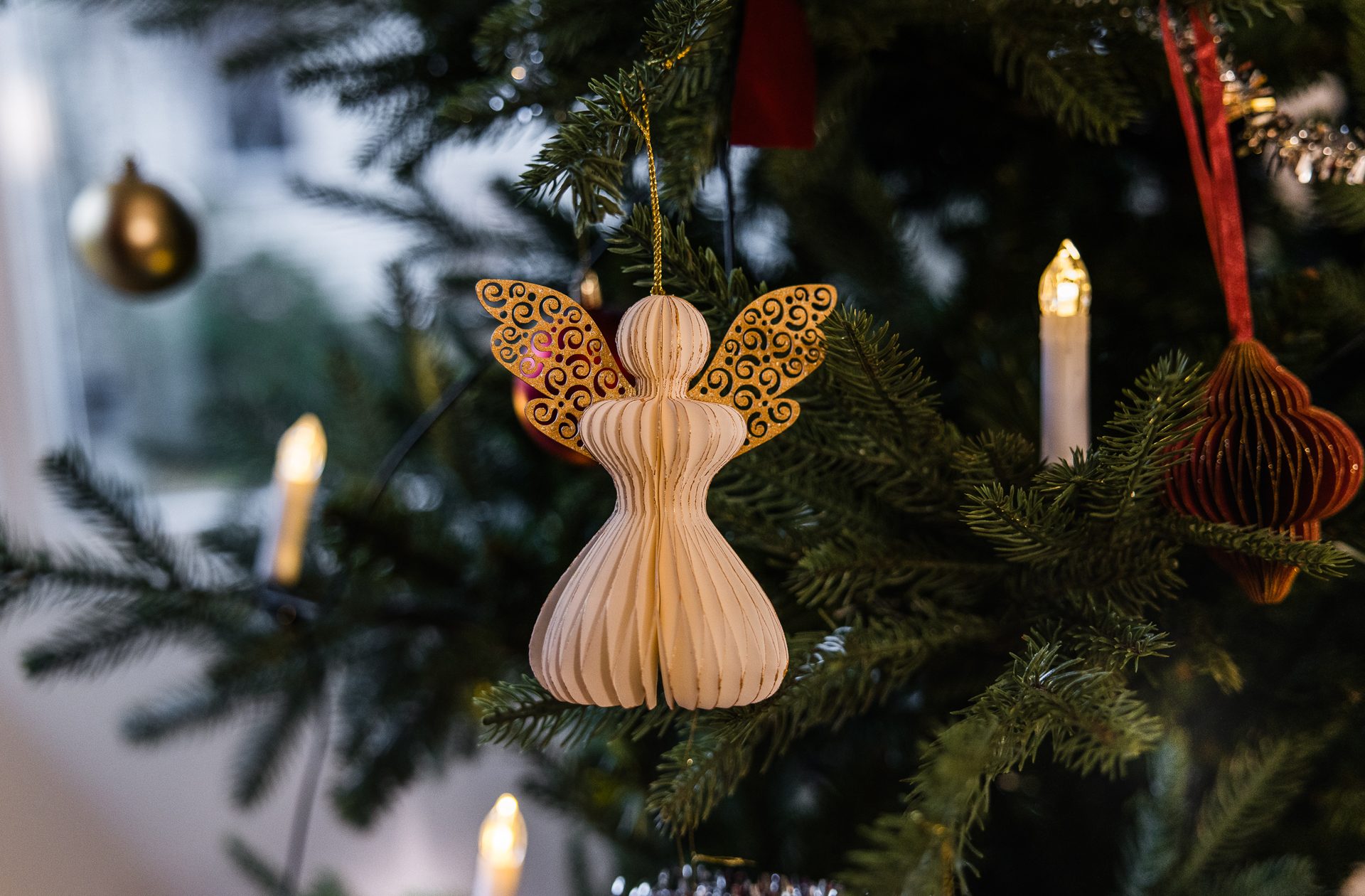 Christmas tree decorated with a paper angel, glowing lights, a gold bauble, and red ornament.