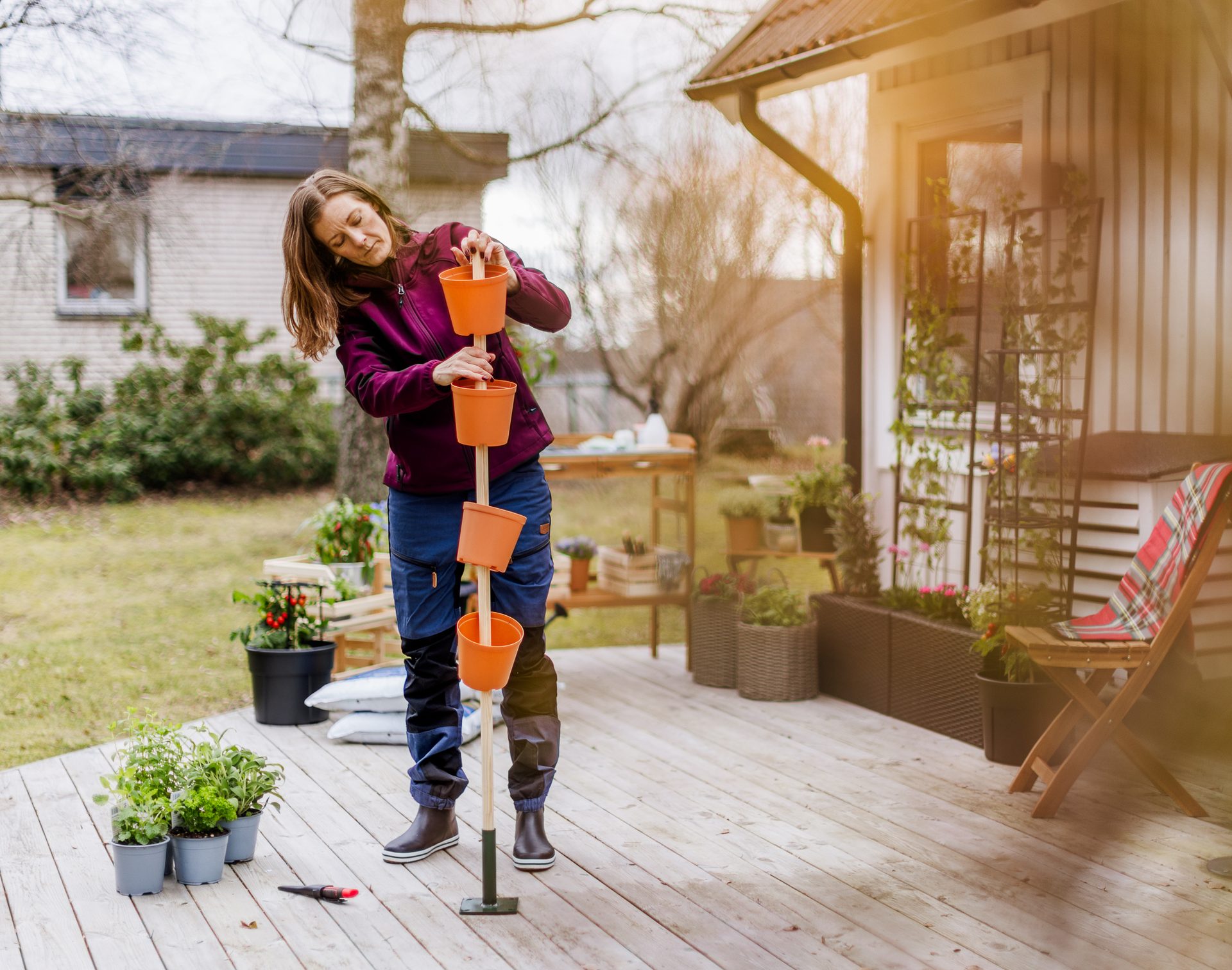 A woman on a deck assembling a vertical garden planter with orange pots, preparing for planting.