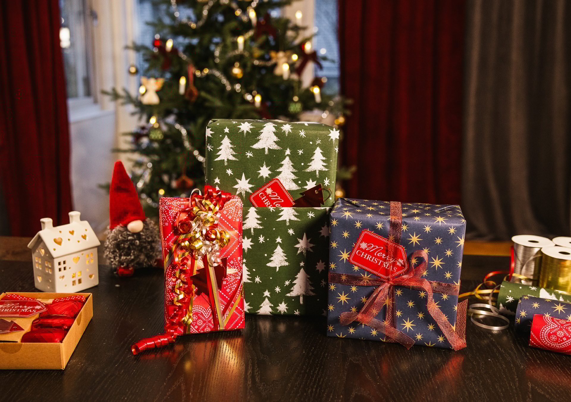 Christmas presents on a table with a decorated tree and festive items in the background.