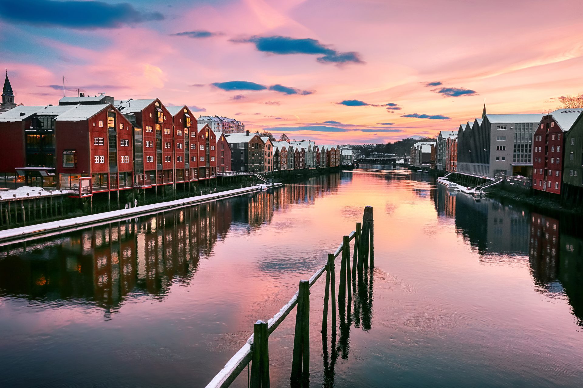 Pink sunset over a snowy river city, with historic red buildings reflecting in the water.