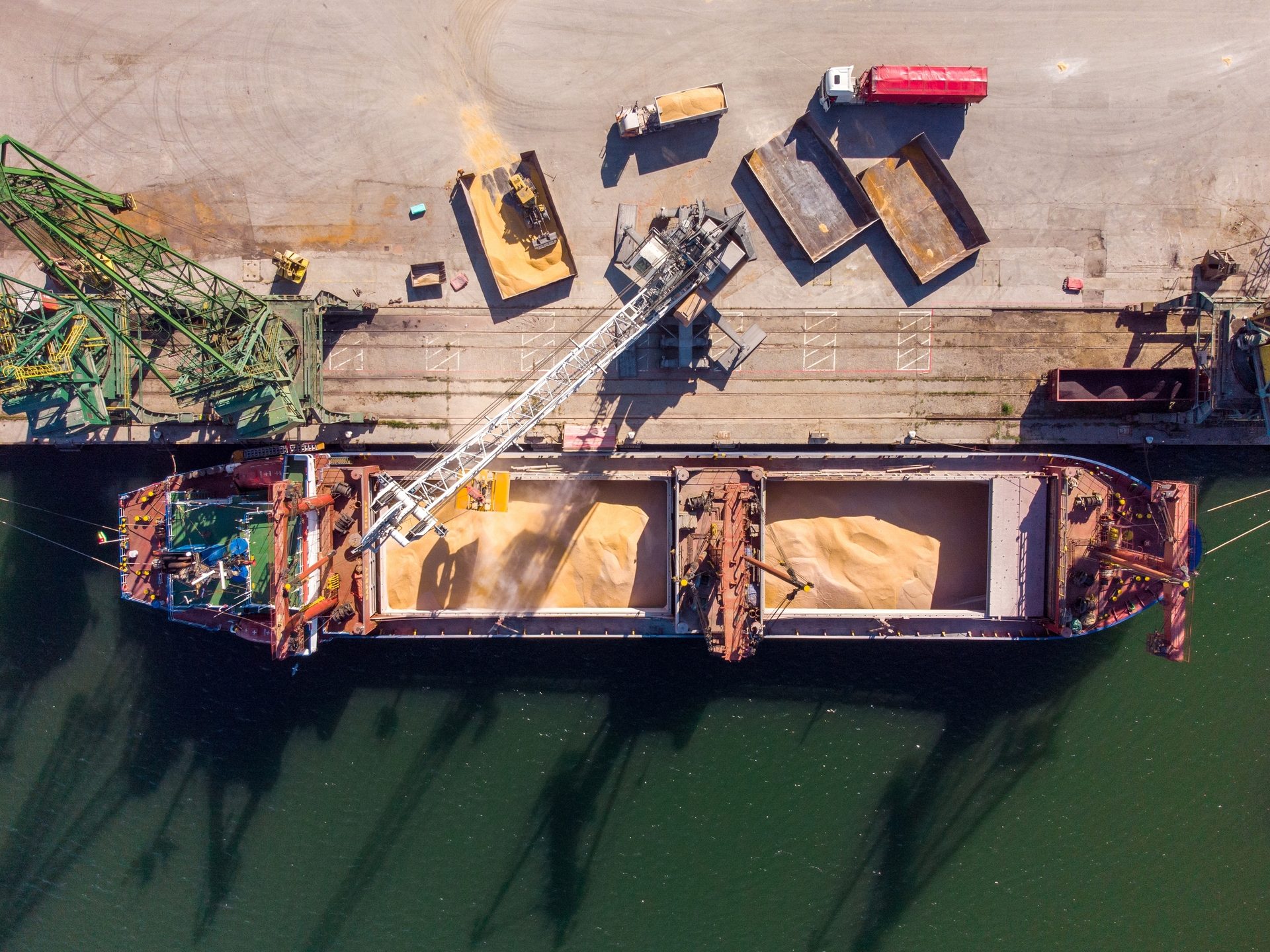 Aerial view: Cargo ship loading grain with a crane at a busy port.