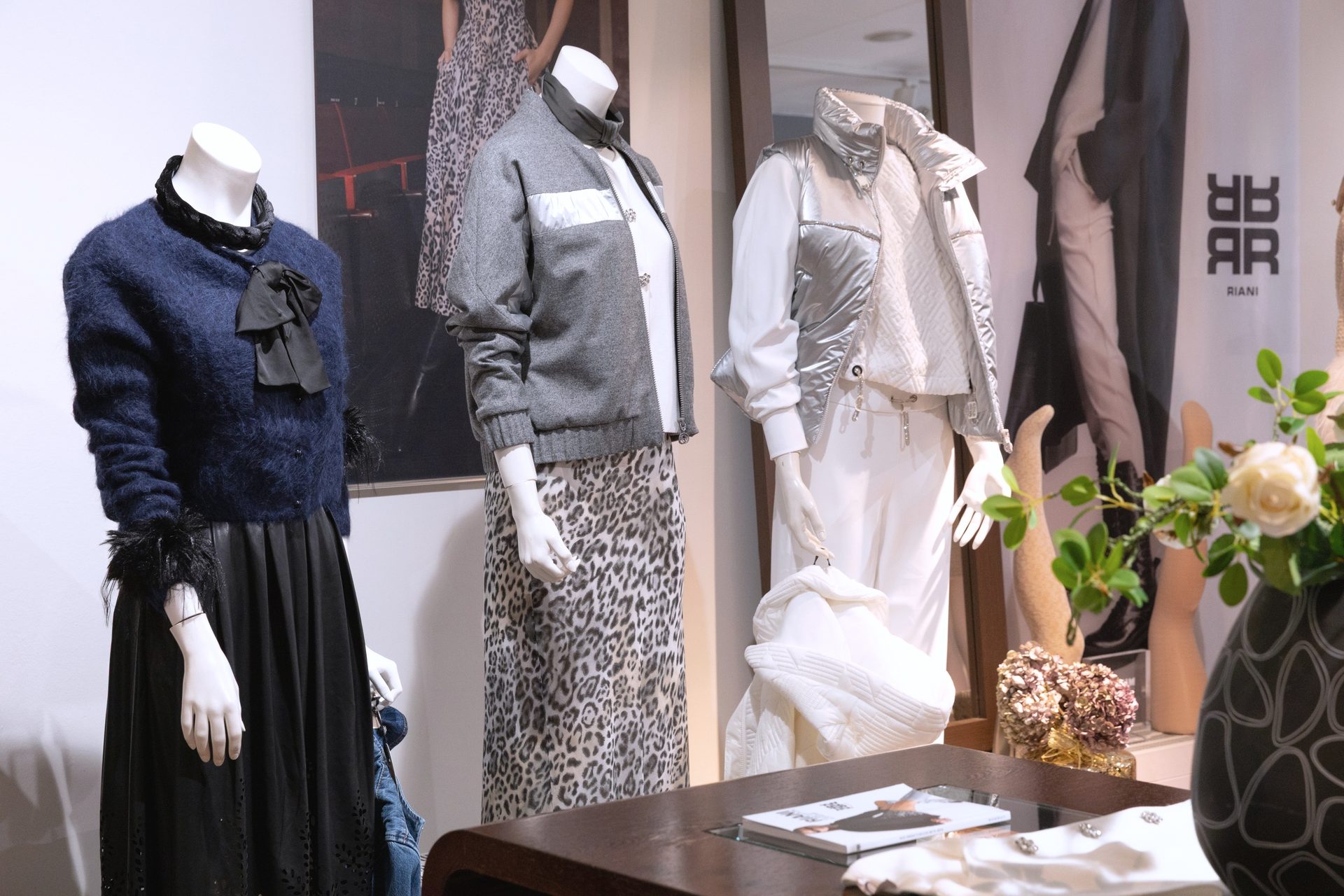 Three mannequins display various outfits: a fuzzy blue top, a leopard print skirt, and a silver puffer vest.