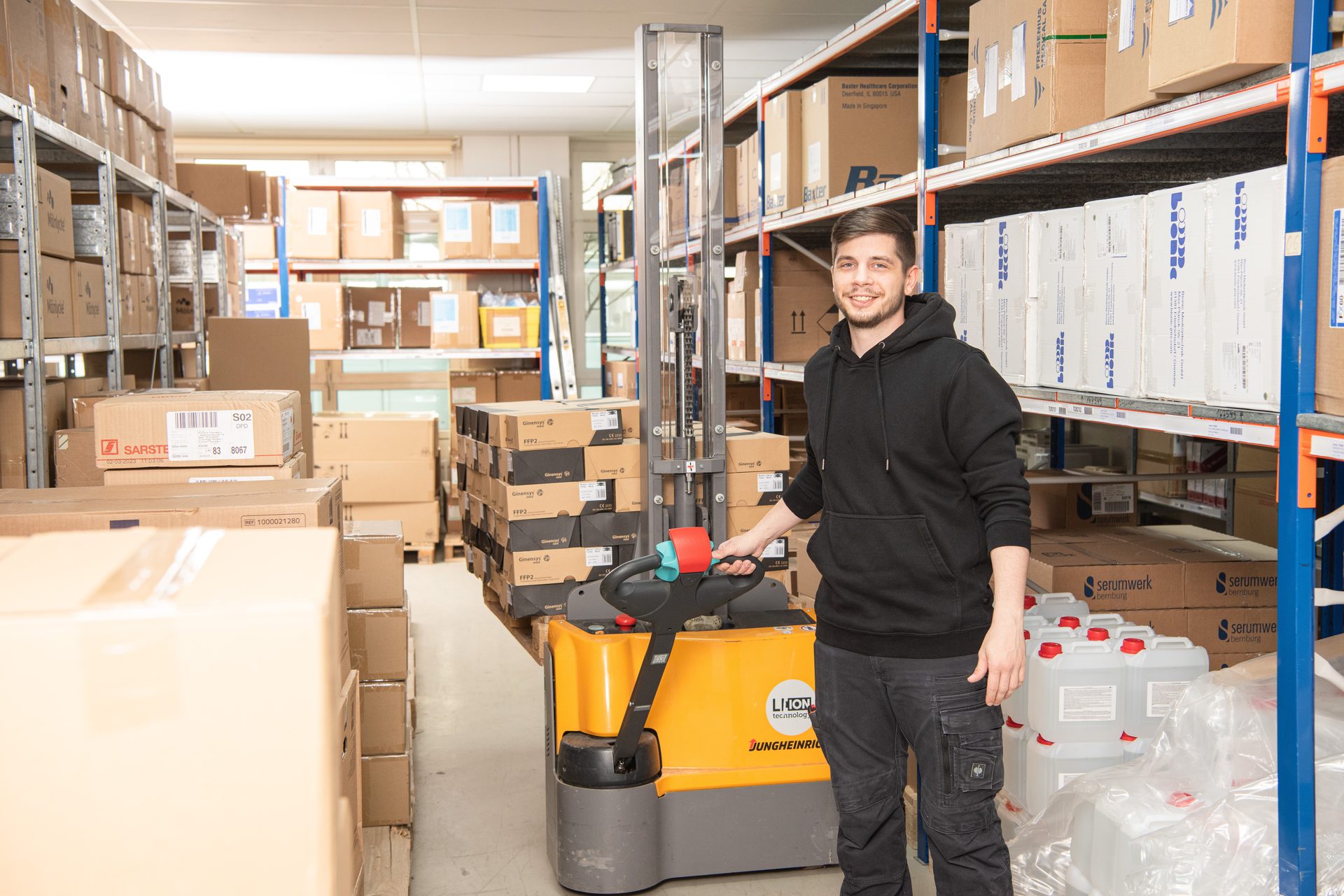Smiling man with a Jungheinrich pallet jack in a warehouse filled with boxes.
