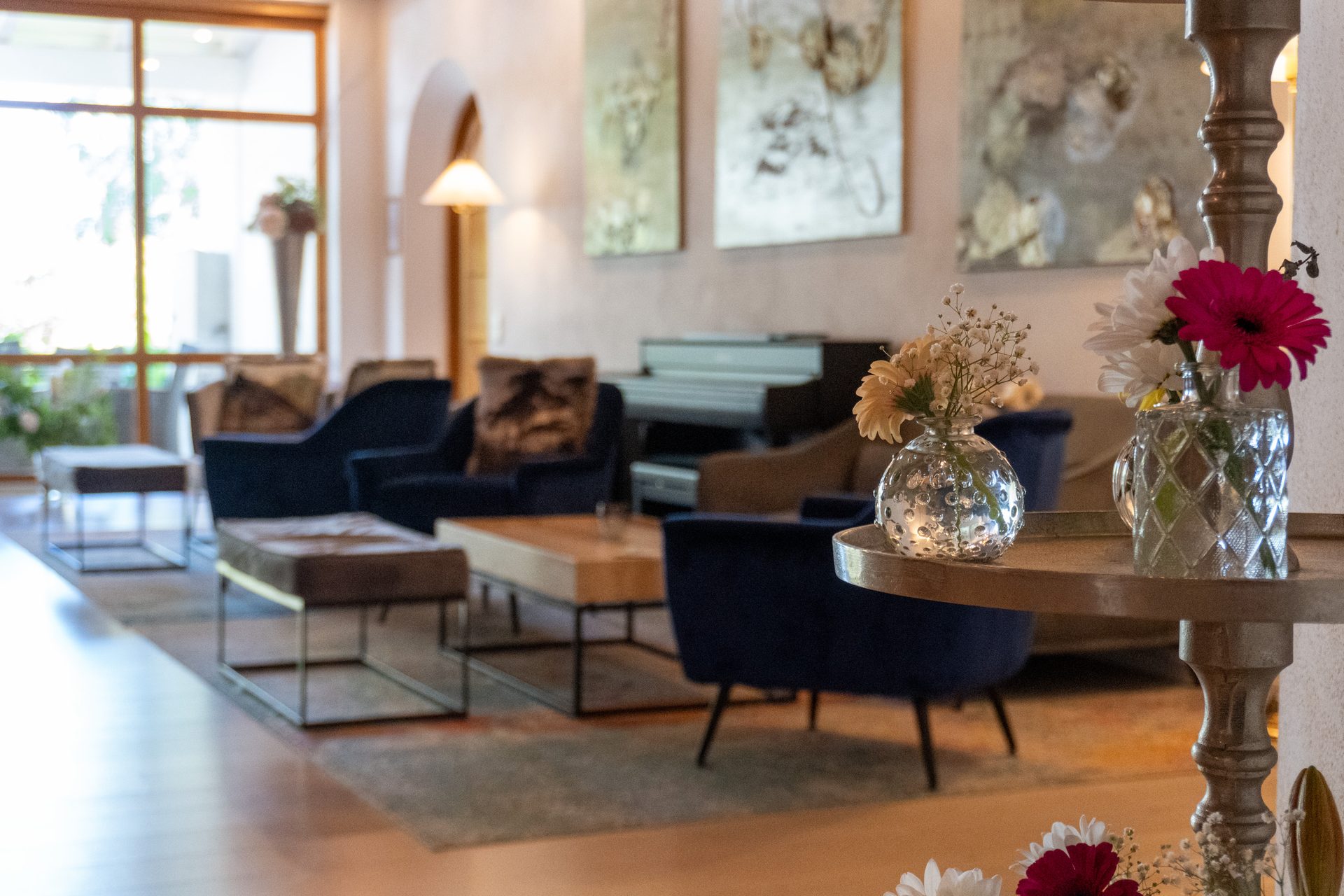 Elegant hotel lobby with seating, piano, art, and flowers on a foreground table.
