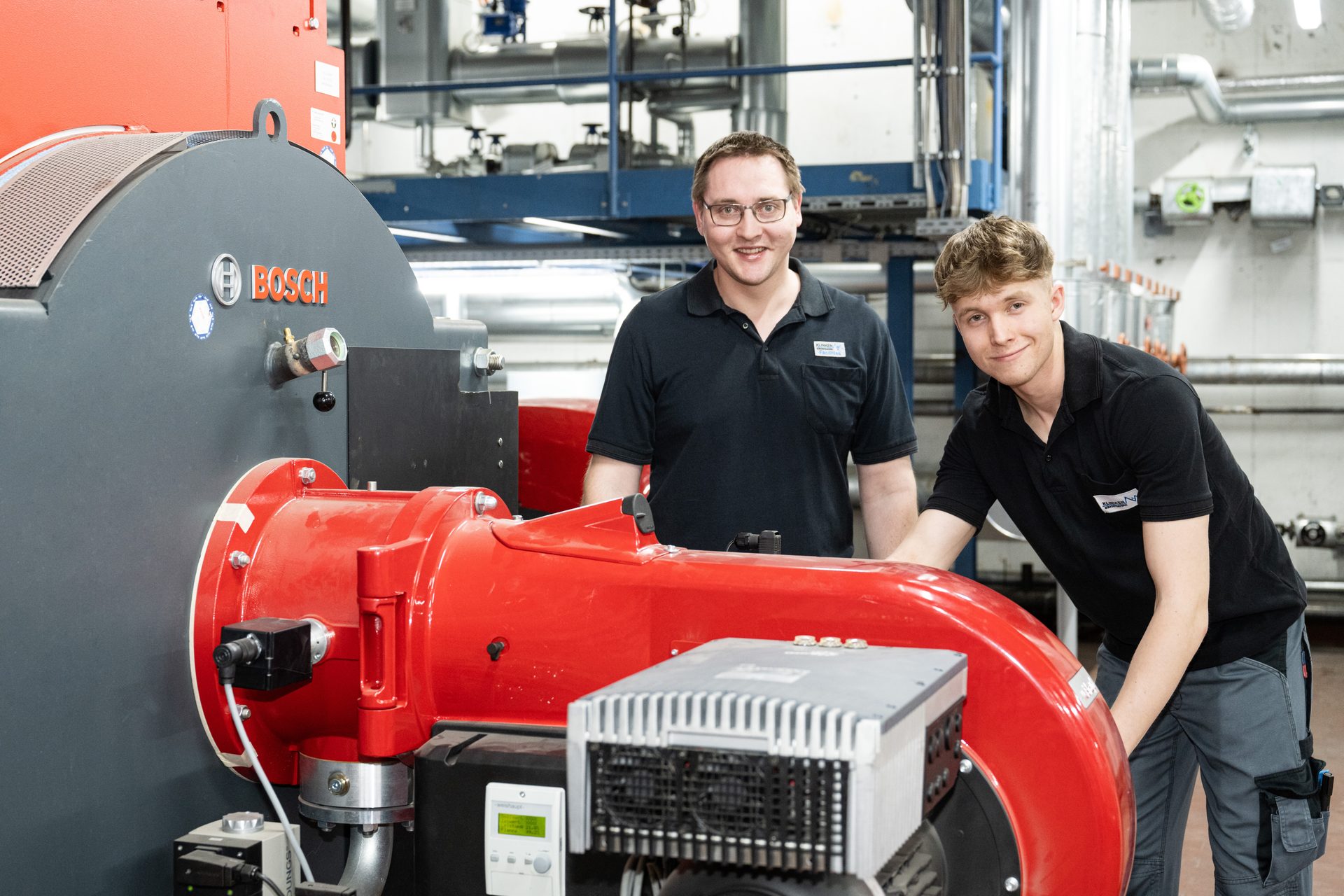 Two smiling men next to a Bosch industrial boiler.