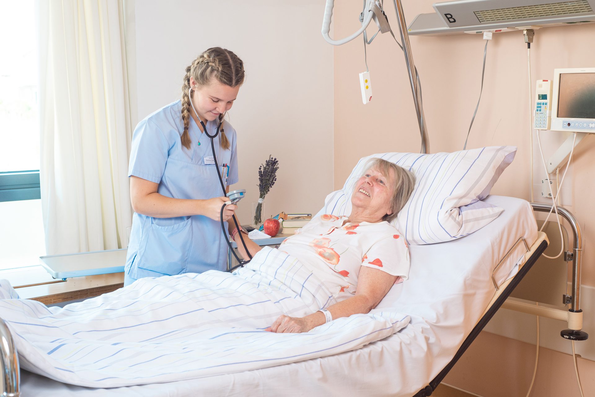 A nurse takes an elderly patient's blood pressure in a hospital bed.