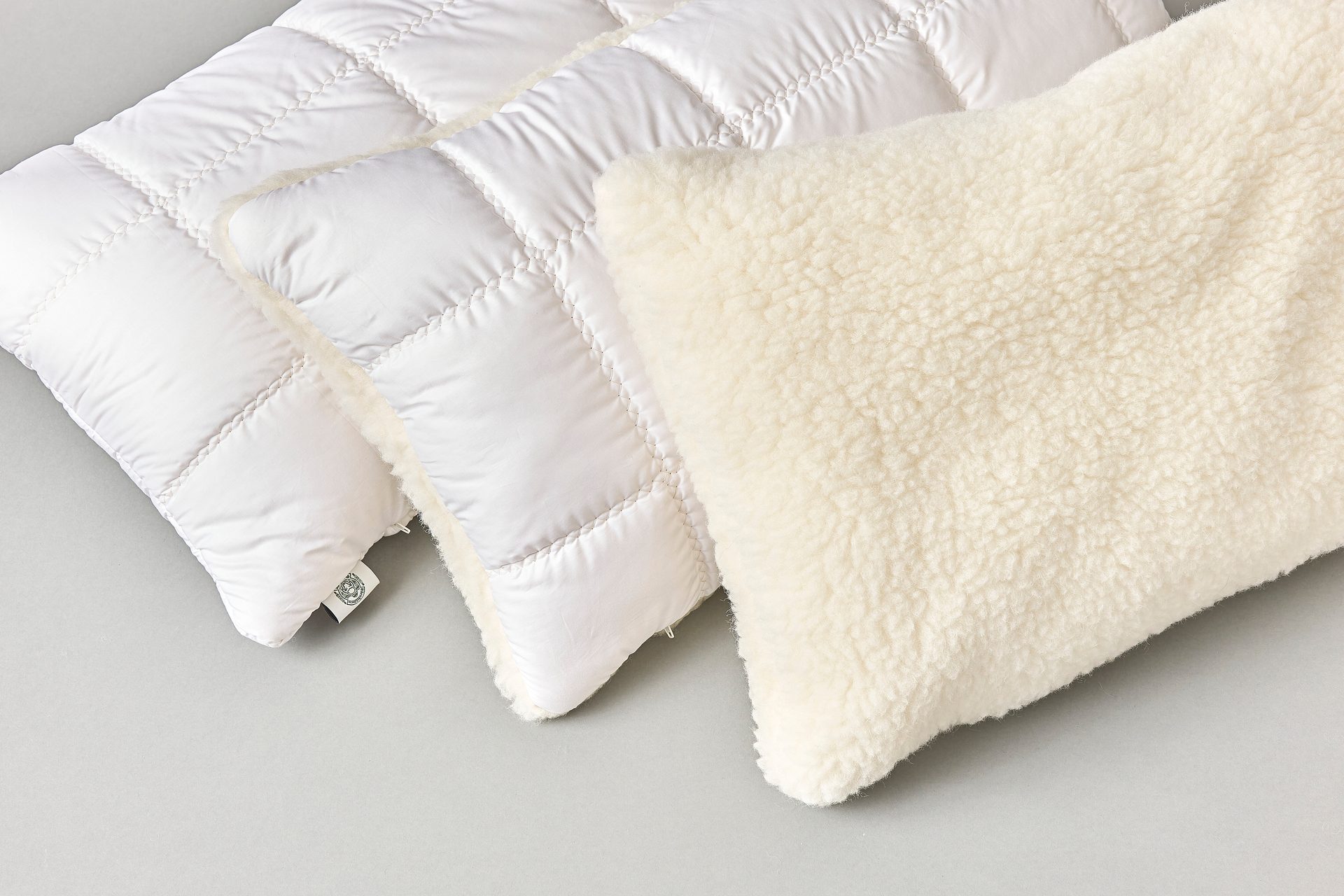 Two white quilted cushions and one cream fluffy cushion on a grey background.