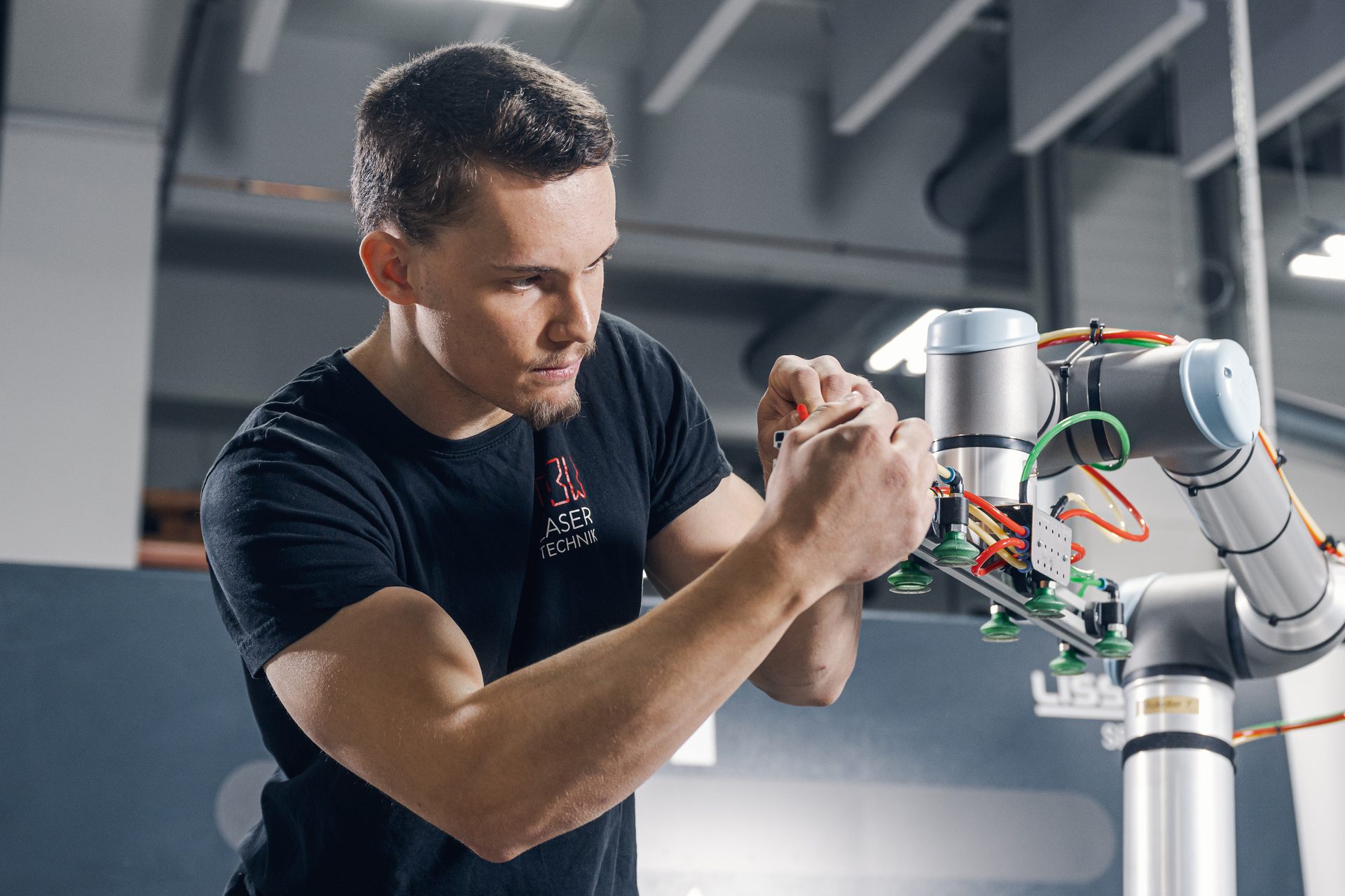Man adjusting a robotic arm with colorful wires.