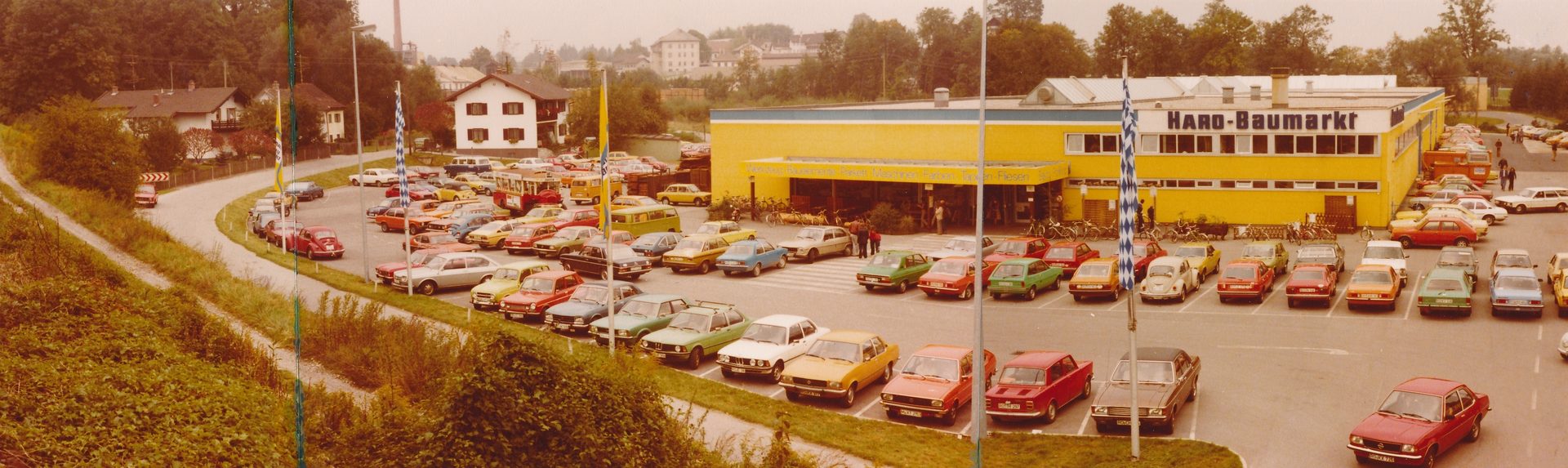 A vibrant 1970s "HAUS-BAUMARKT" hardware store with a busy parking lot filled with vintage cars.