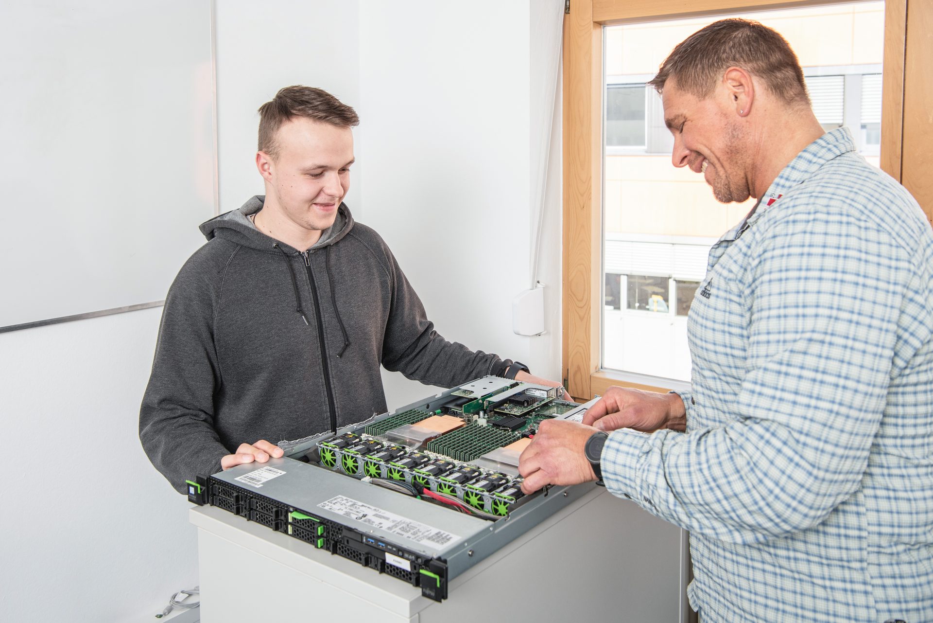 Two men smiling and working together on an open server.