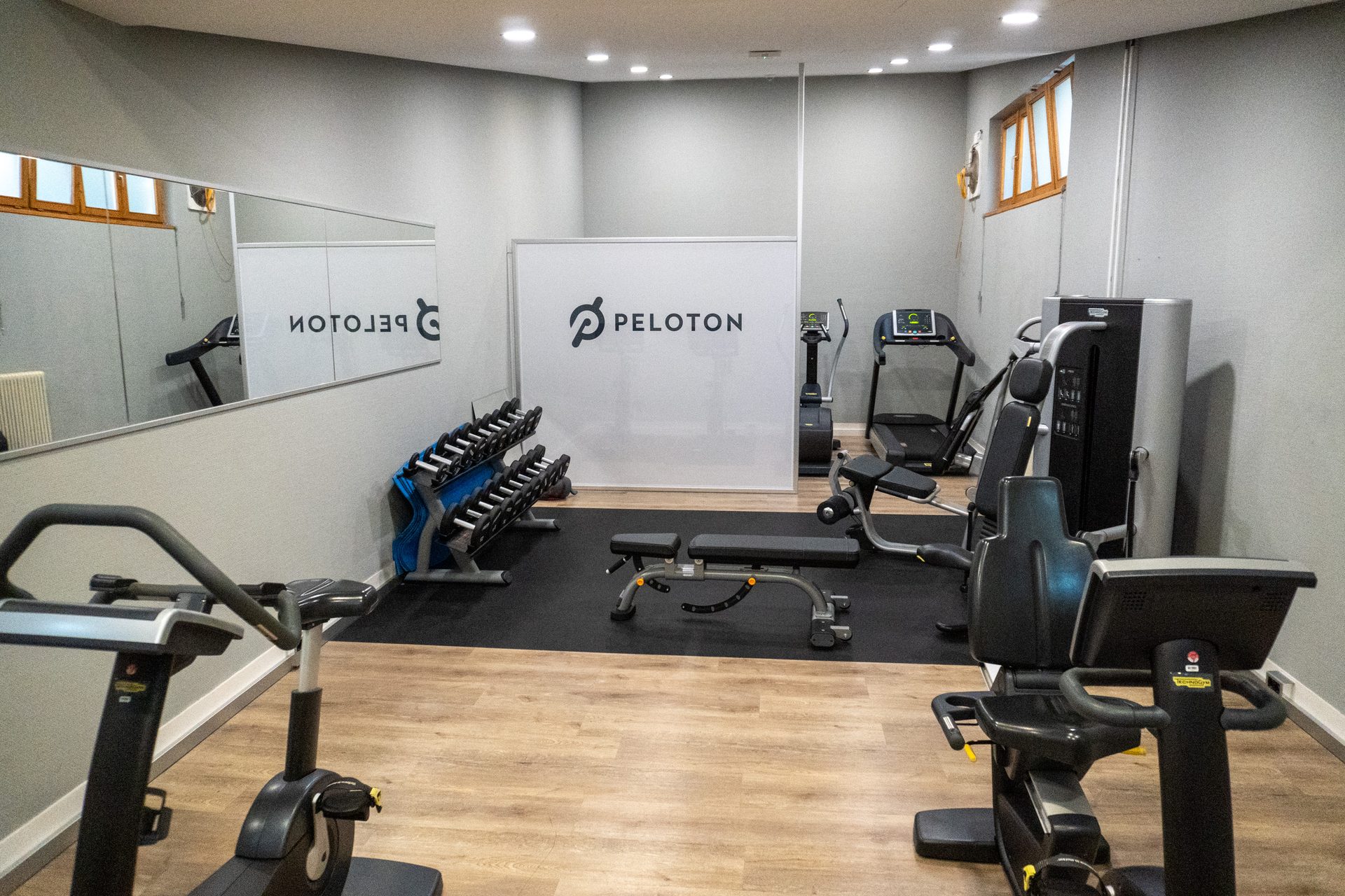 Peloton gym interior: exercise bikes, treadmill, weights, and dumbbell rack.