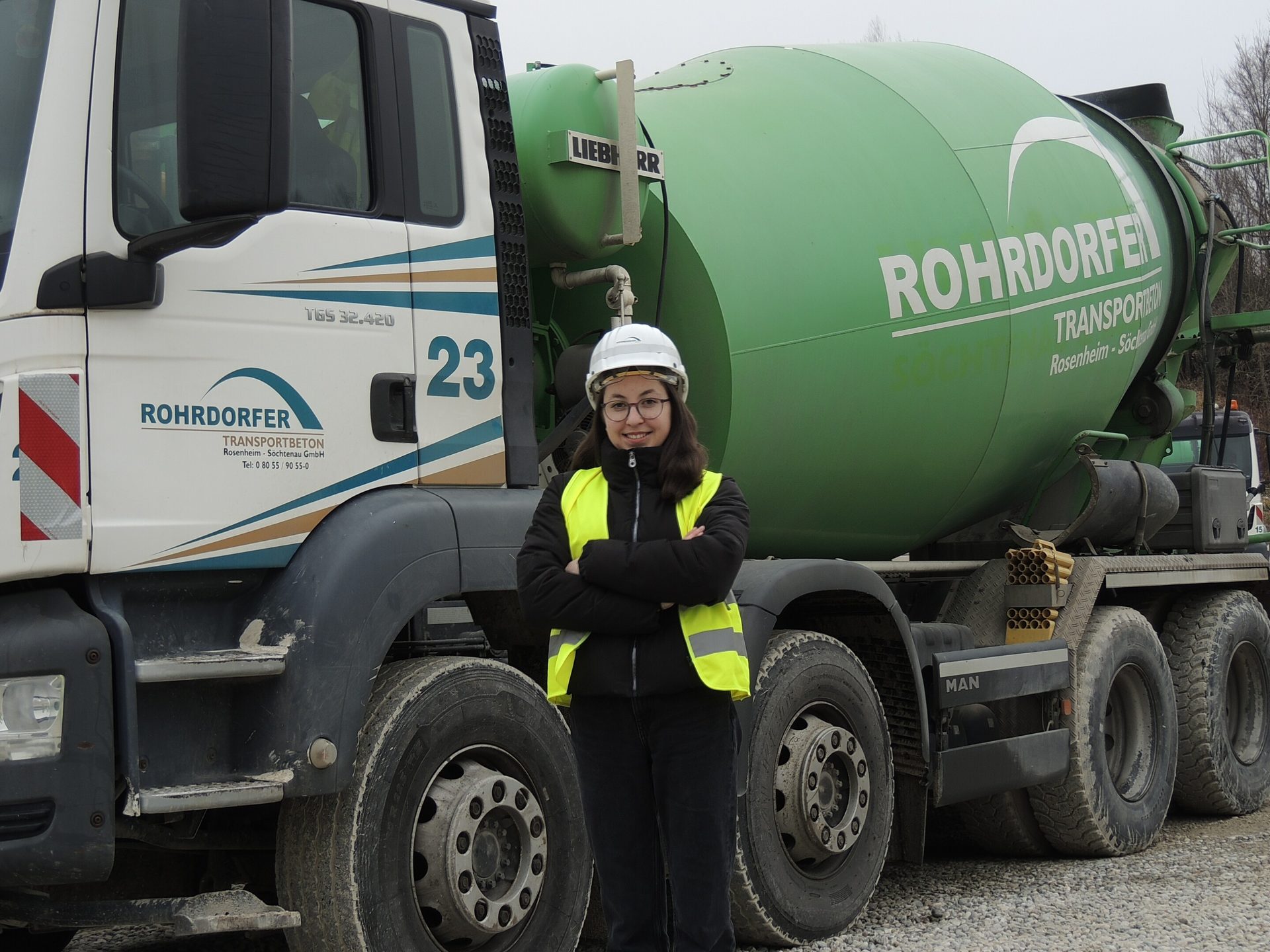 Woman in hard hat and safety vest standing next to a Rohrdorfer cement mixer truck.