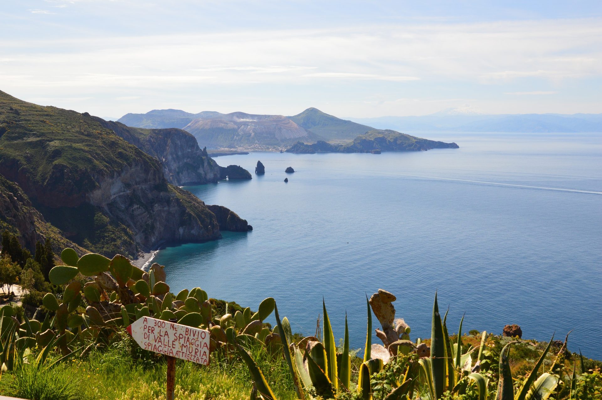 Panoramic view of the Aeolian Islands with volcanic peaks, rugged coastline, blue sea, and a direction sign.