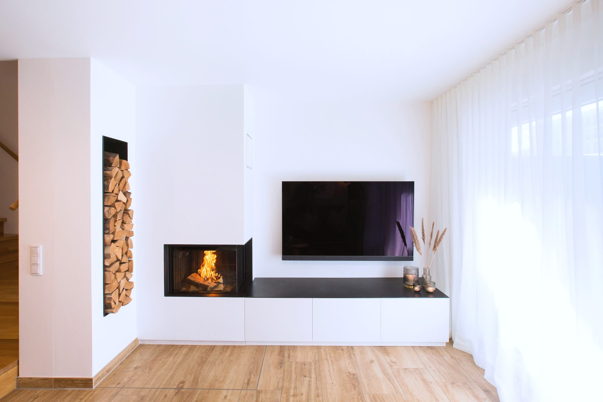 Modern living room with a built-in fireplace, stacked wood, wall-mounted TV, white console, and wood floor.