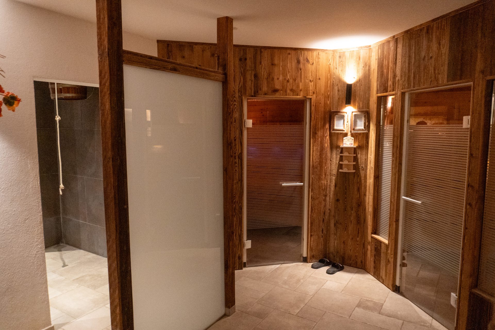 Warm-lit spa area with rustic wooden walls, frosted glass doors to saunas, and a shower.