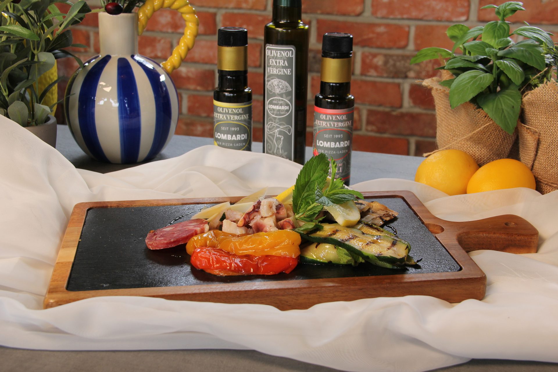 A platter of seafood, grilled vegetables, cured meat, and cheese, with olive oil bottles and lemons.