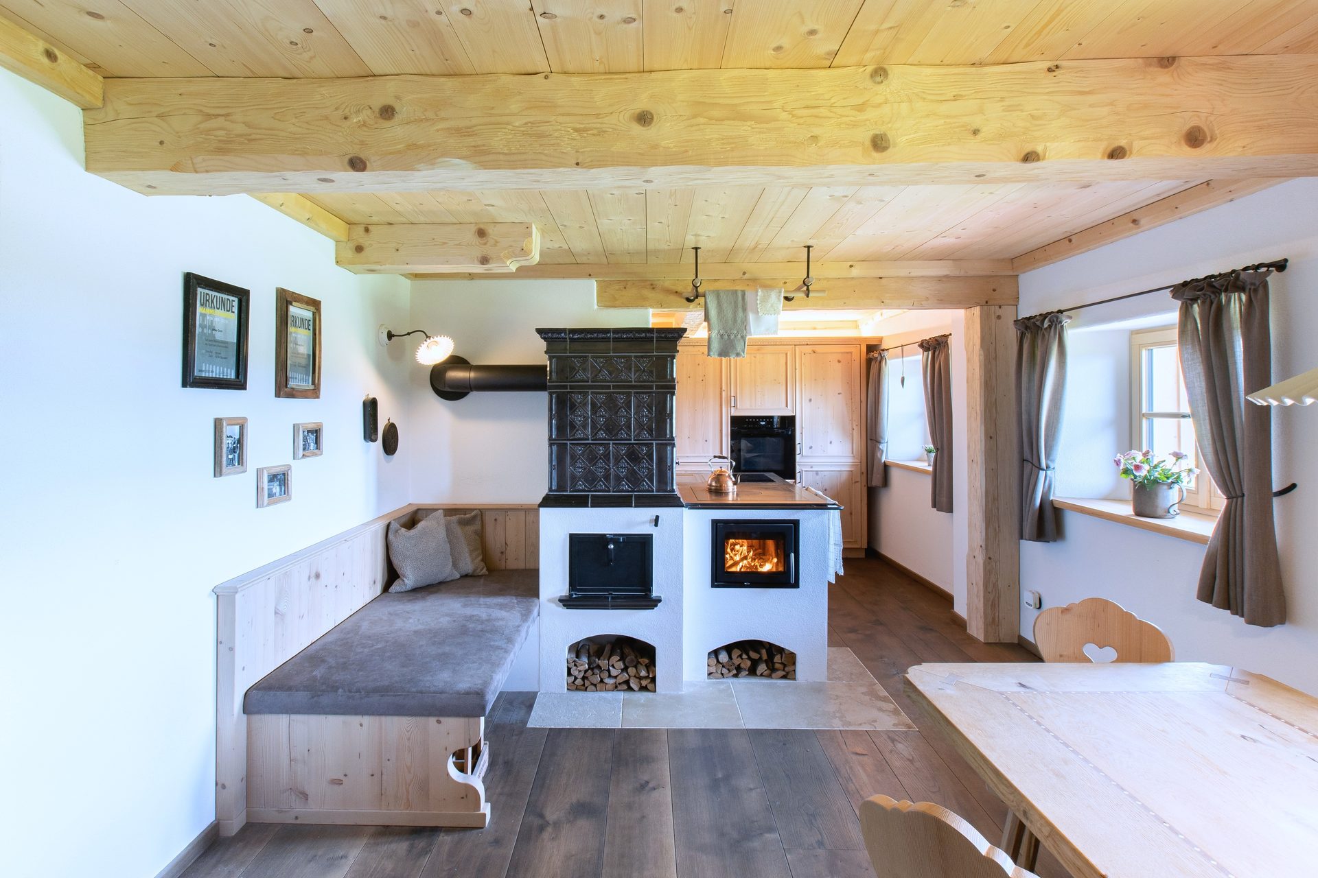 Rustic kitchen-dining room with wooden elements, a traditional tiled stove, built-in bench, and dining table.