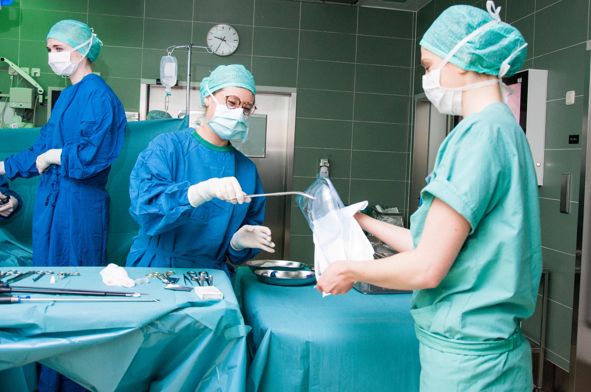 Three medical staff in scrubs and masks preparing instruments in an operating room.