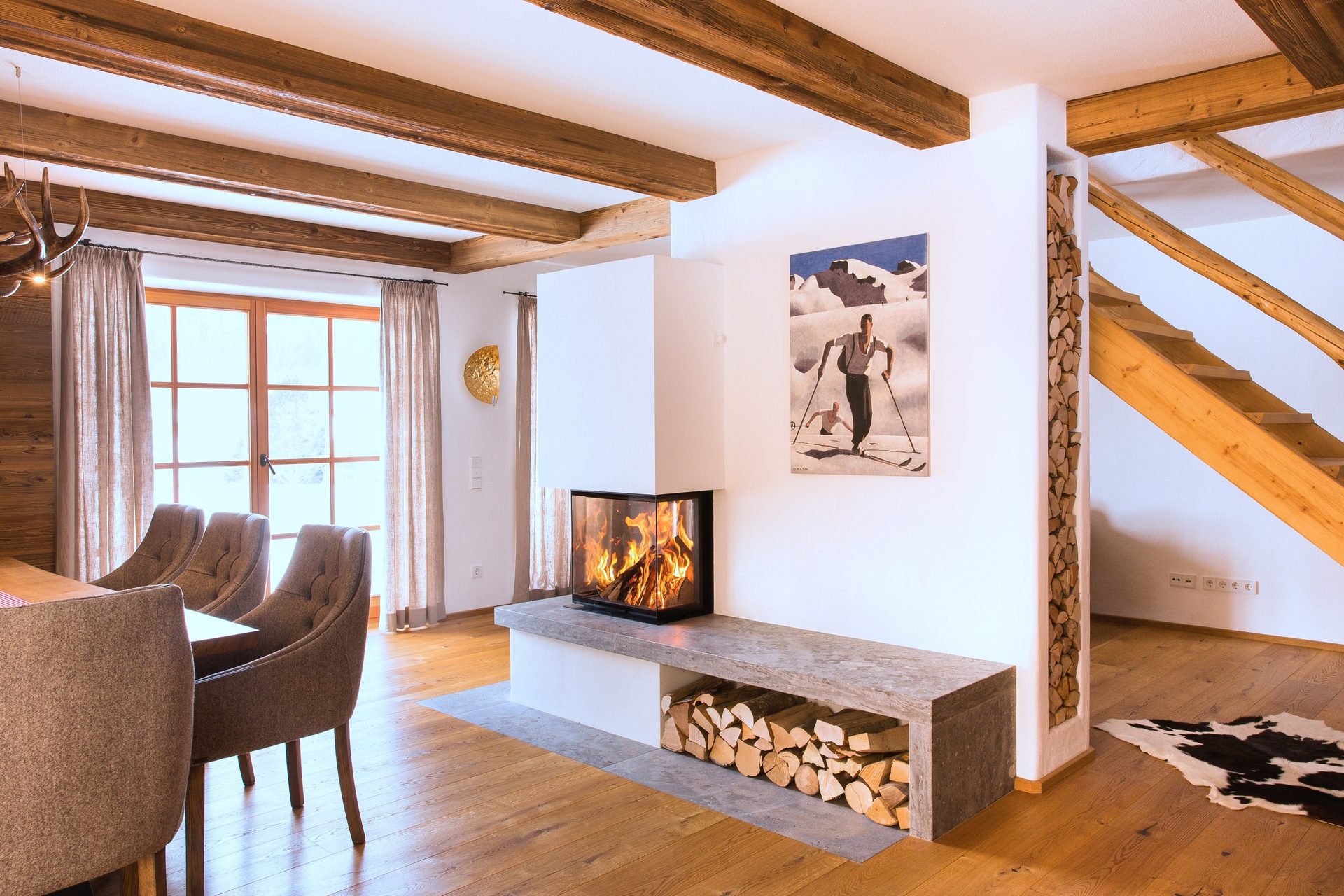 Modern rustic living room with a fireplace, wood beams, a dining table, and a staircase.