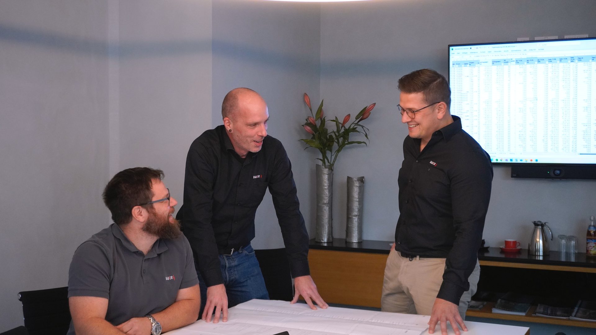 Three smiling men discussing documents at a table in an office meeting.