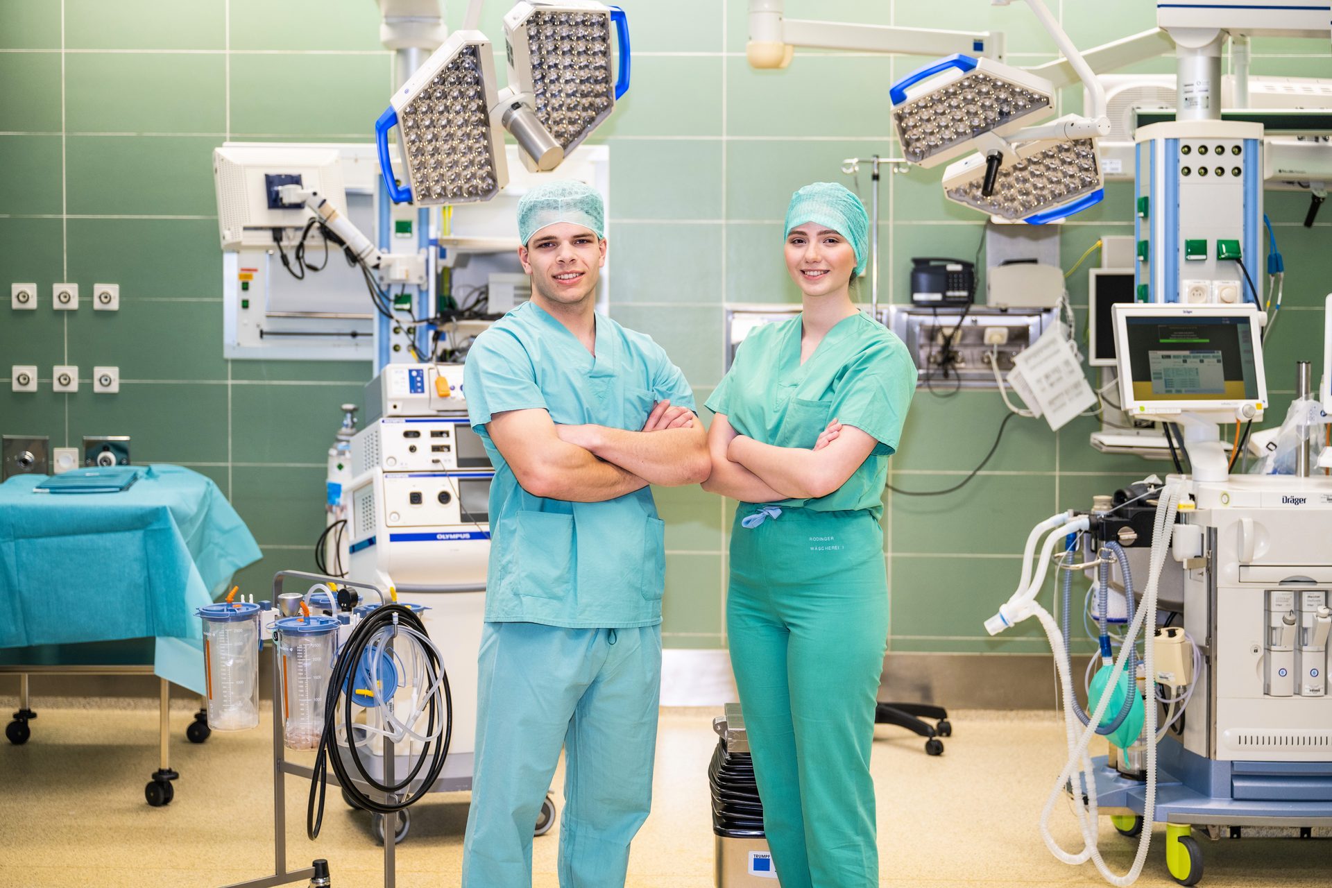 Two smiling surgeons in scrubs standing in an operating room with medical equipment.