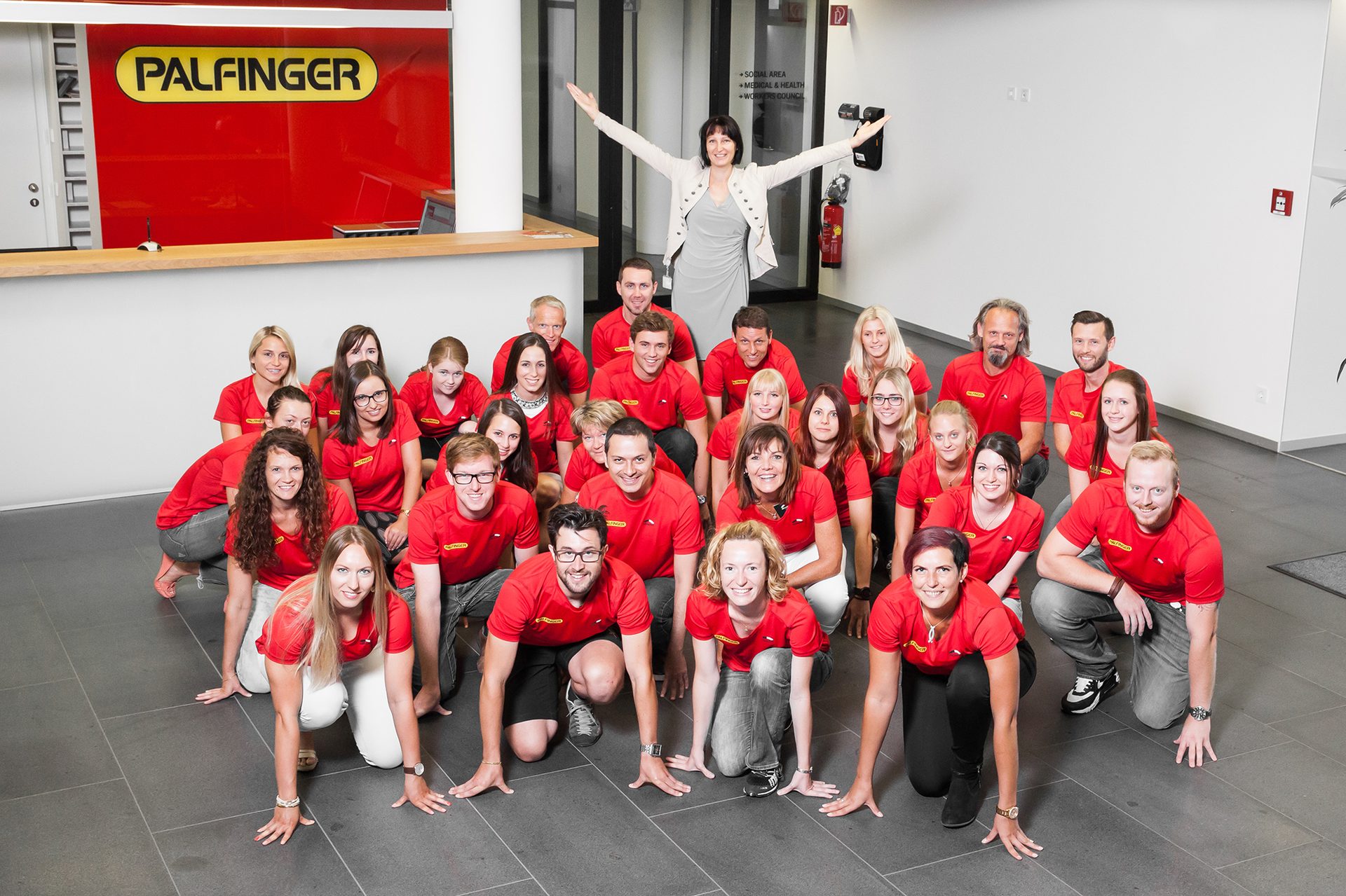 Palfinger team in red shirts, mostly kneeling, one woman stands arms outstretched.