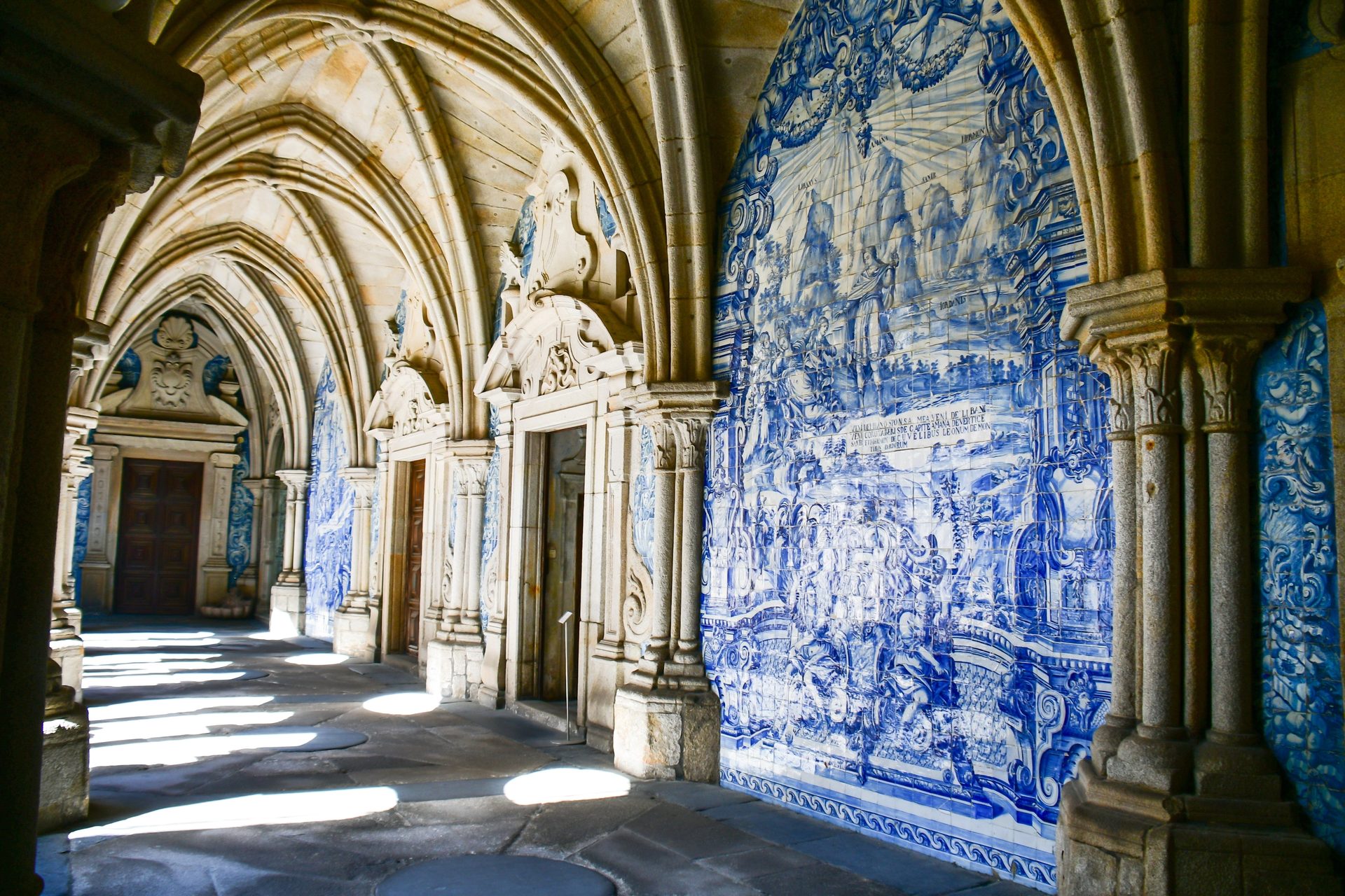 A long, arched stone hallway adorned with intricate blue and white azulejo tiles on the right wall.