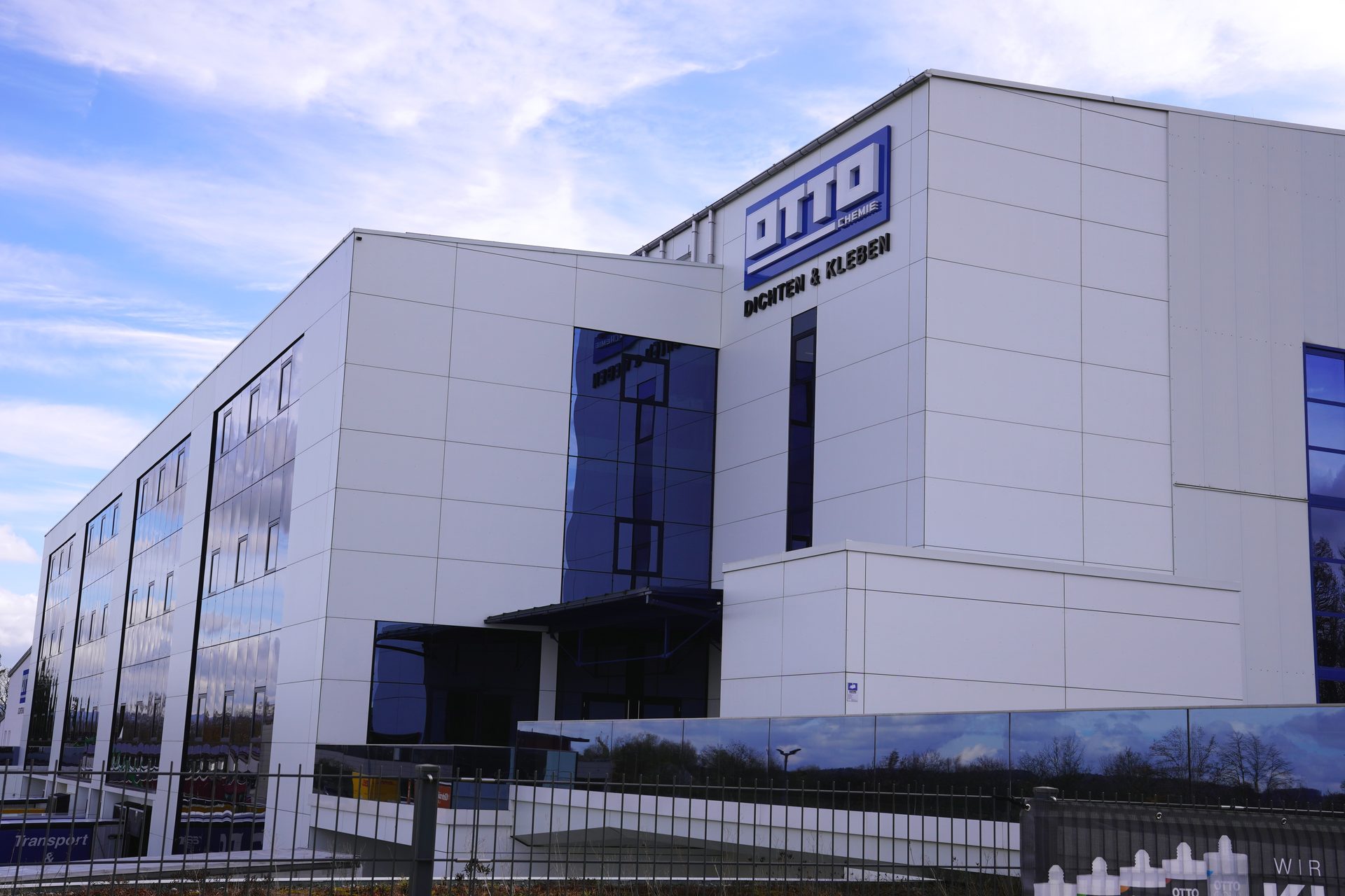Modern Otto Chemie building with blue glass windows and white facade under a bright sky.