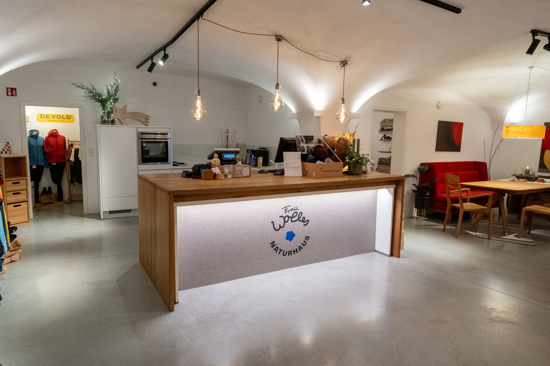 Warmly lit, vaulted interior of a "Frau Wolle Naturhaus" store with a wooden counter, clothing, and seating.
