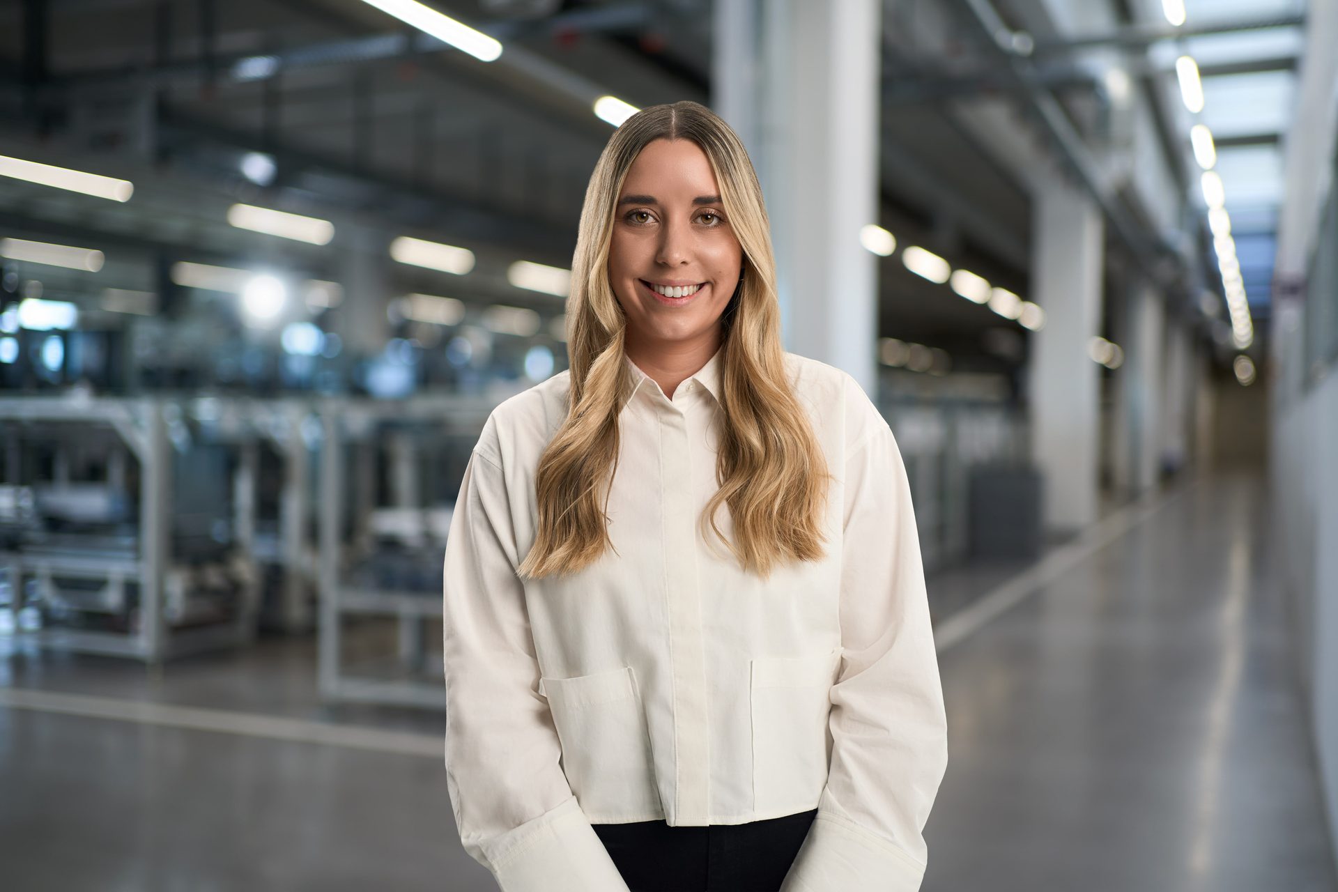 Smiling woman in a light shirt in a modern factory setting.