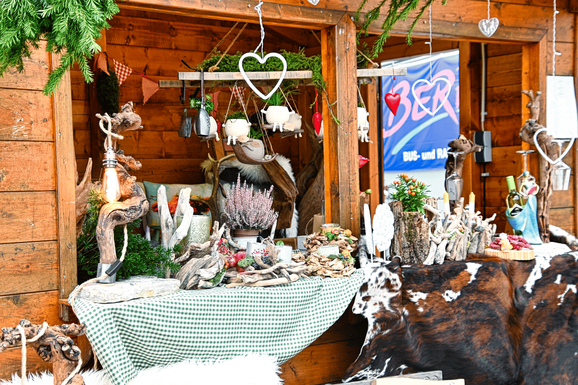Rustic wooden stall decorated with festive plants, driftwood, lights, and hanging heart ornaments.