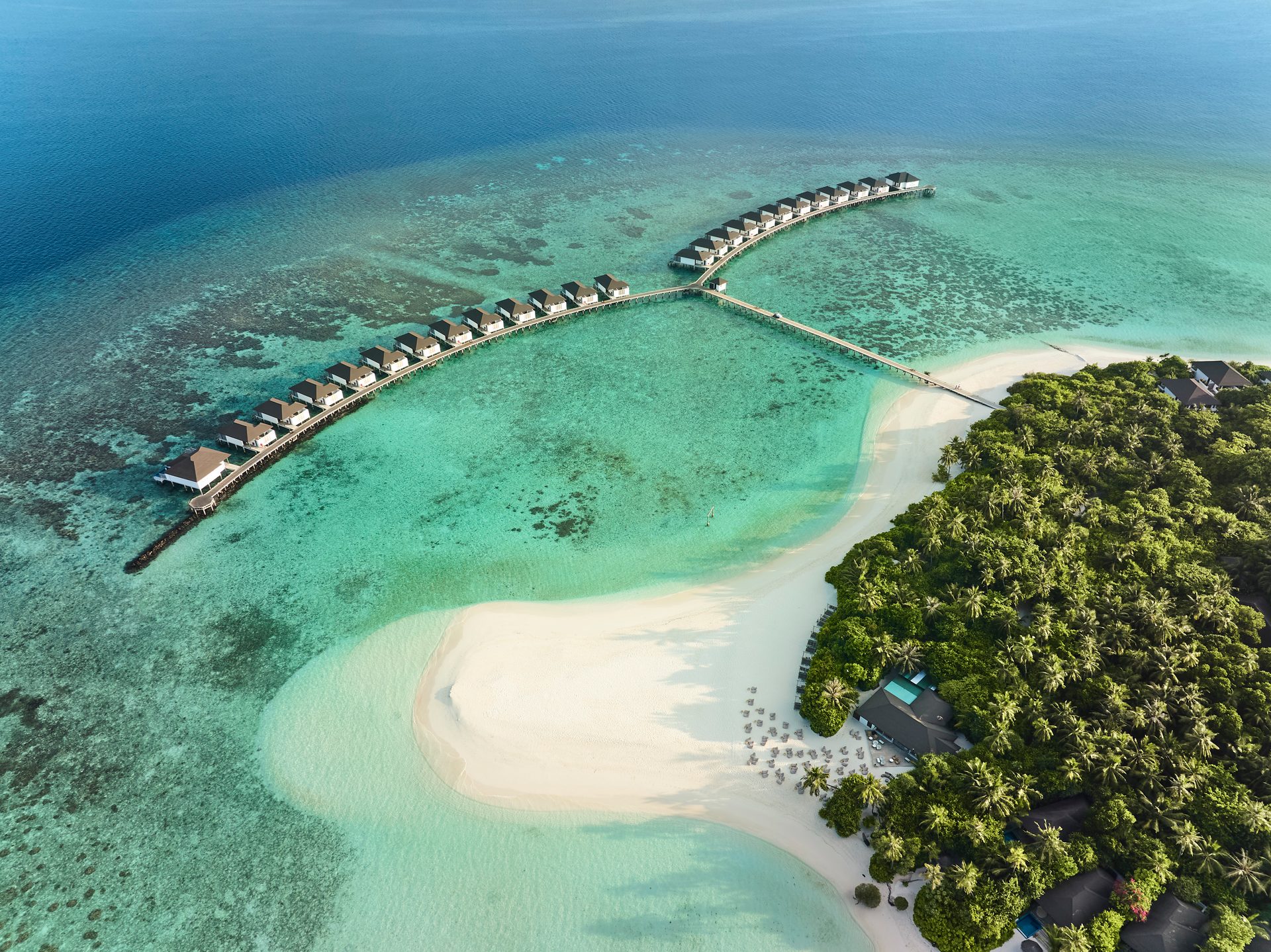 Tropical island resort from above: overwater bungalows, white sand beach, and clear turquoise sea.