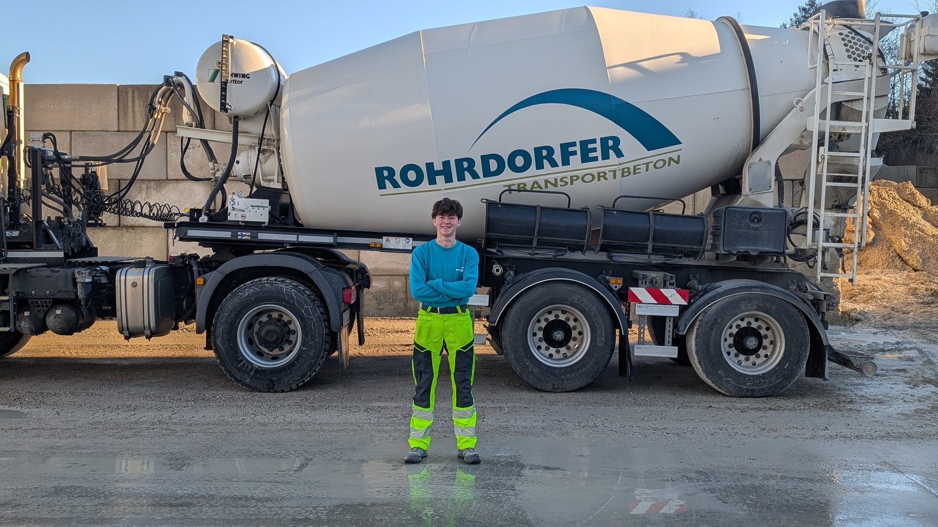 Young man smiling in front of a Rohrdorfer concrete mixer truck.